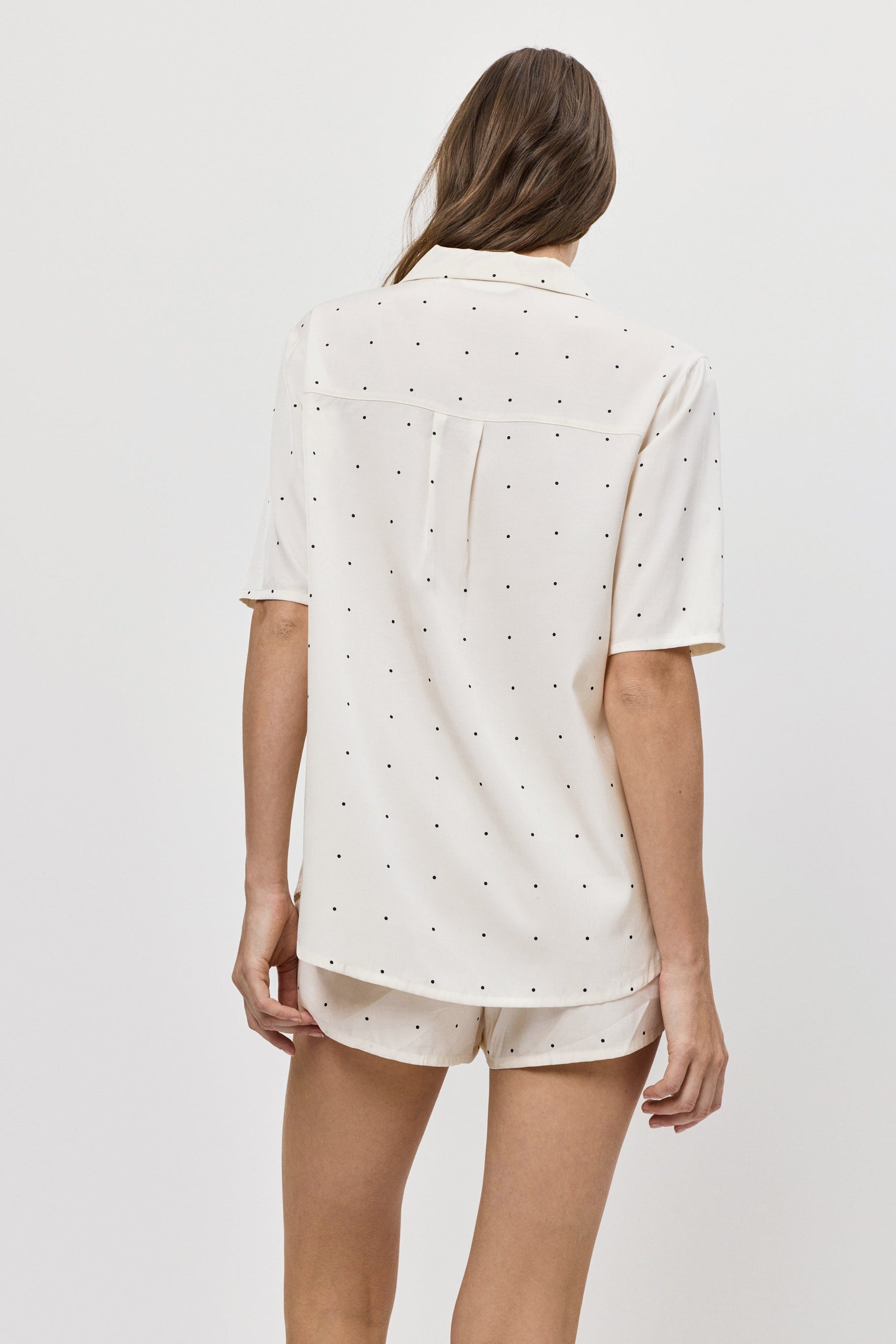 Woman wearing a white polka dot pajama set with shorts on a plain background