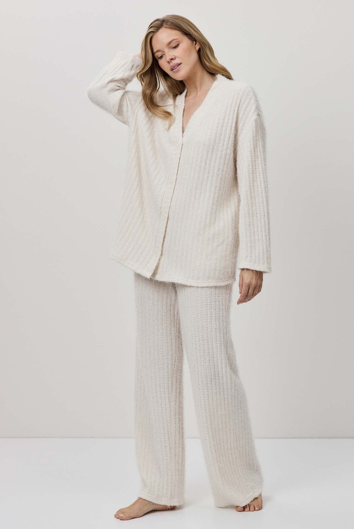 Woman wearing a white ribbed pajama set against a white background