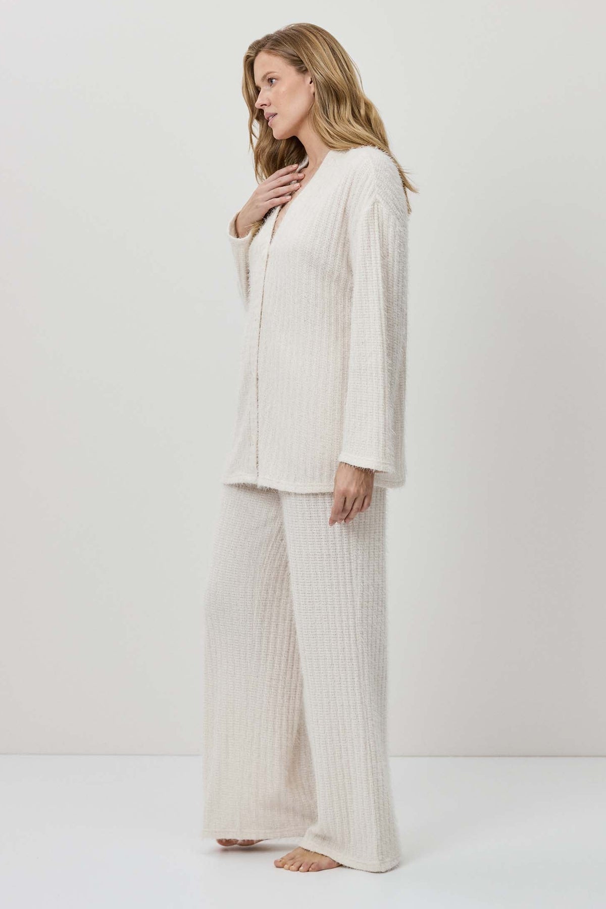 Woman wearing a white outfit with wide-leg pants against a plain background