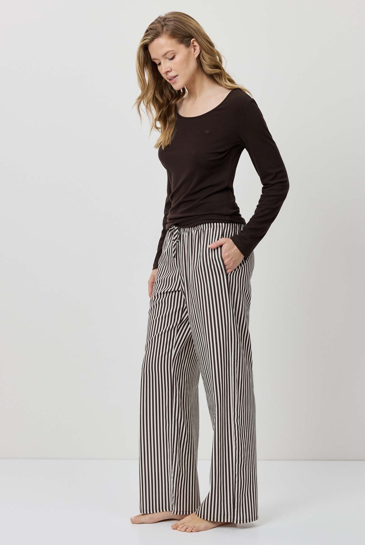Woman wearing a black long-sleeve top and striped pants on a white background