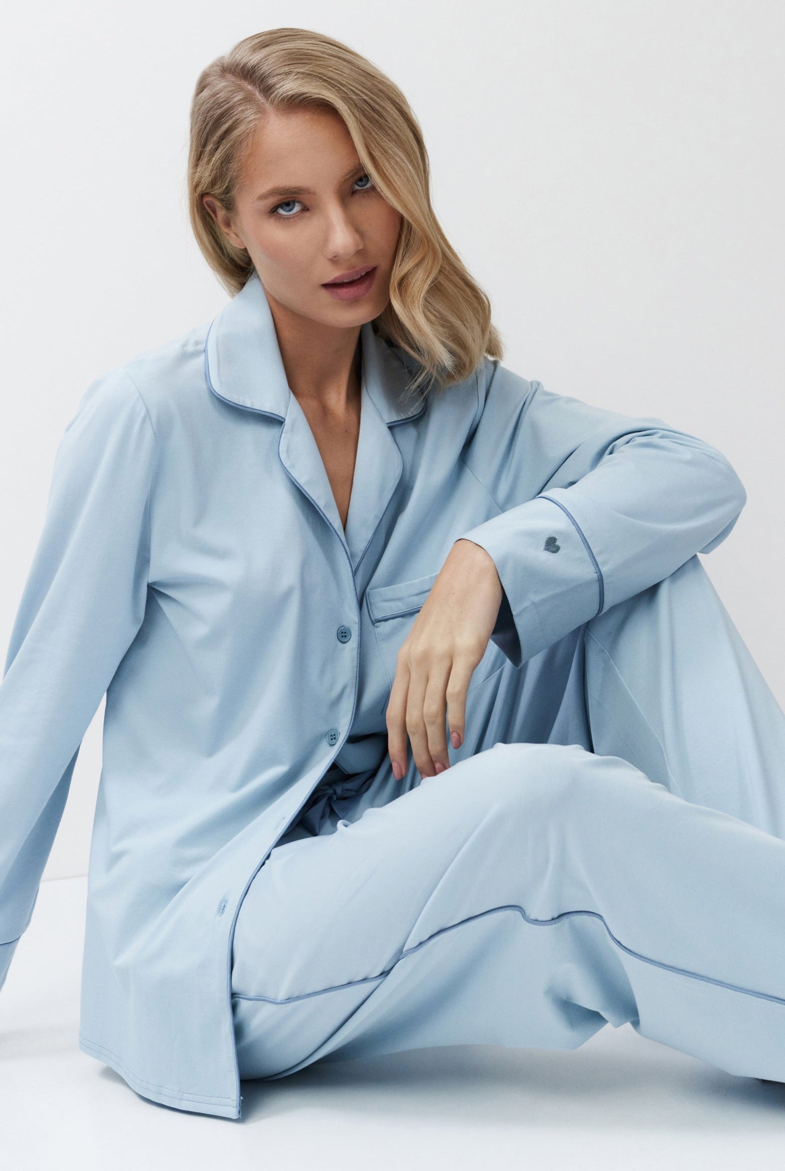 Woman wearing a light blue pajama set sitting on a white background