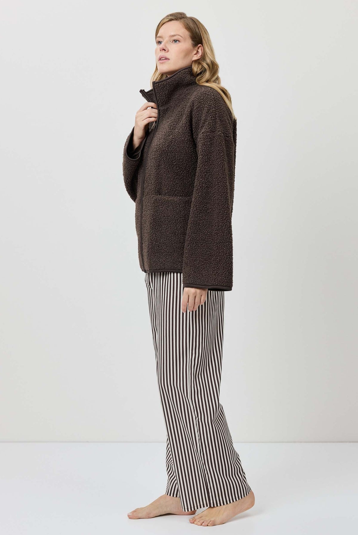 Woman wearing a brown turtleneck sweater and striped pants on a white background