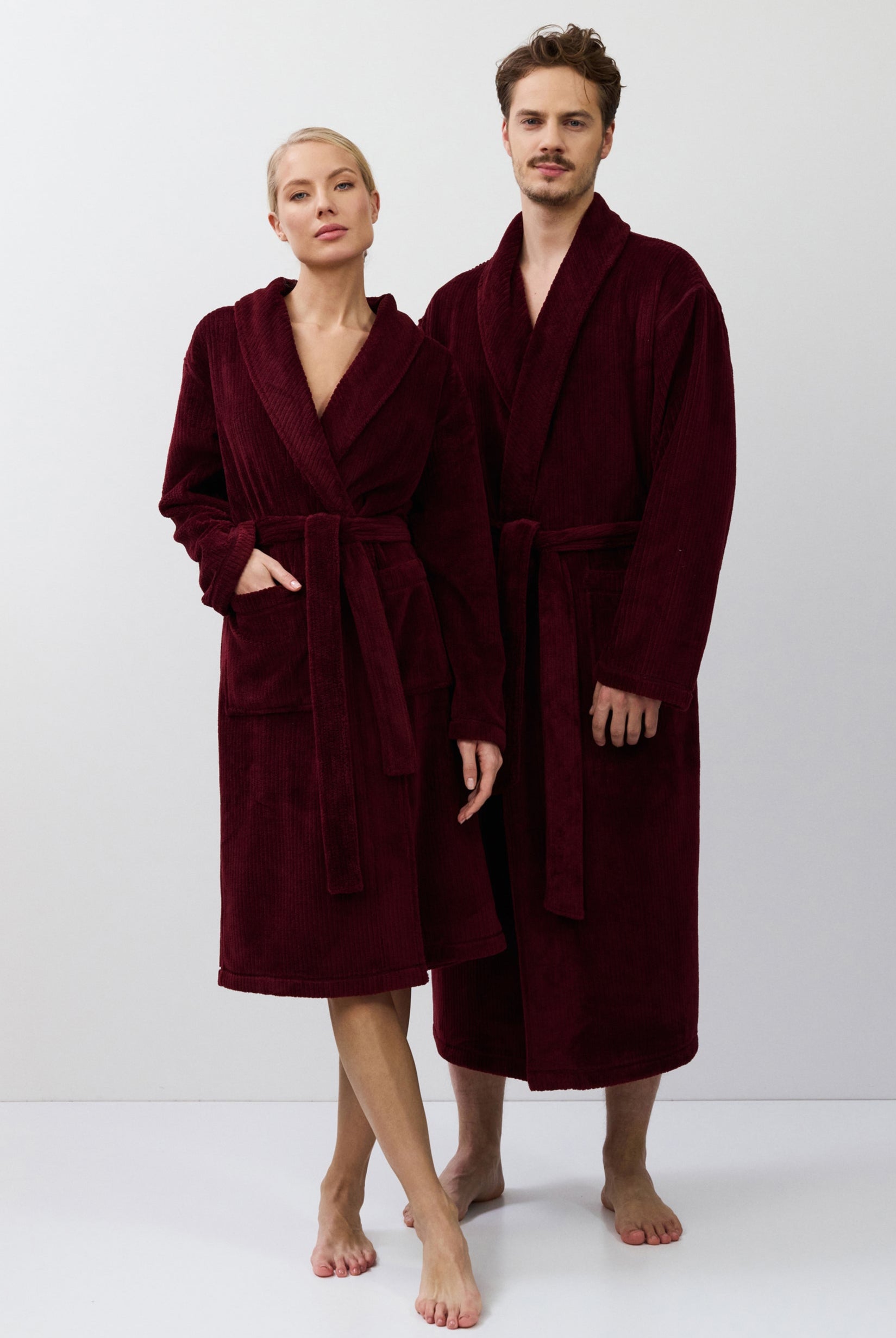 Two people wearing burgundy robes standing side by side on a white background
