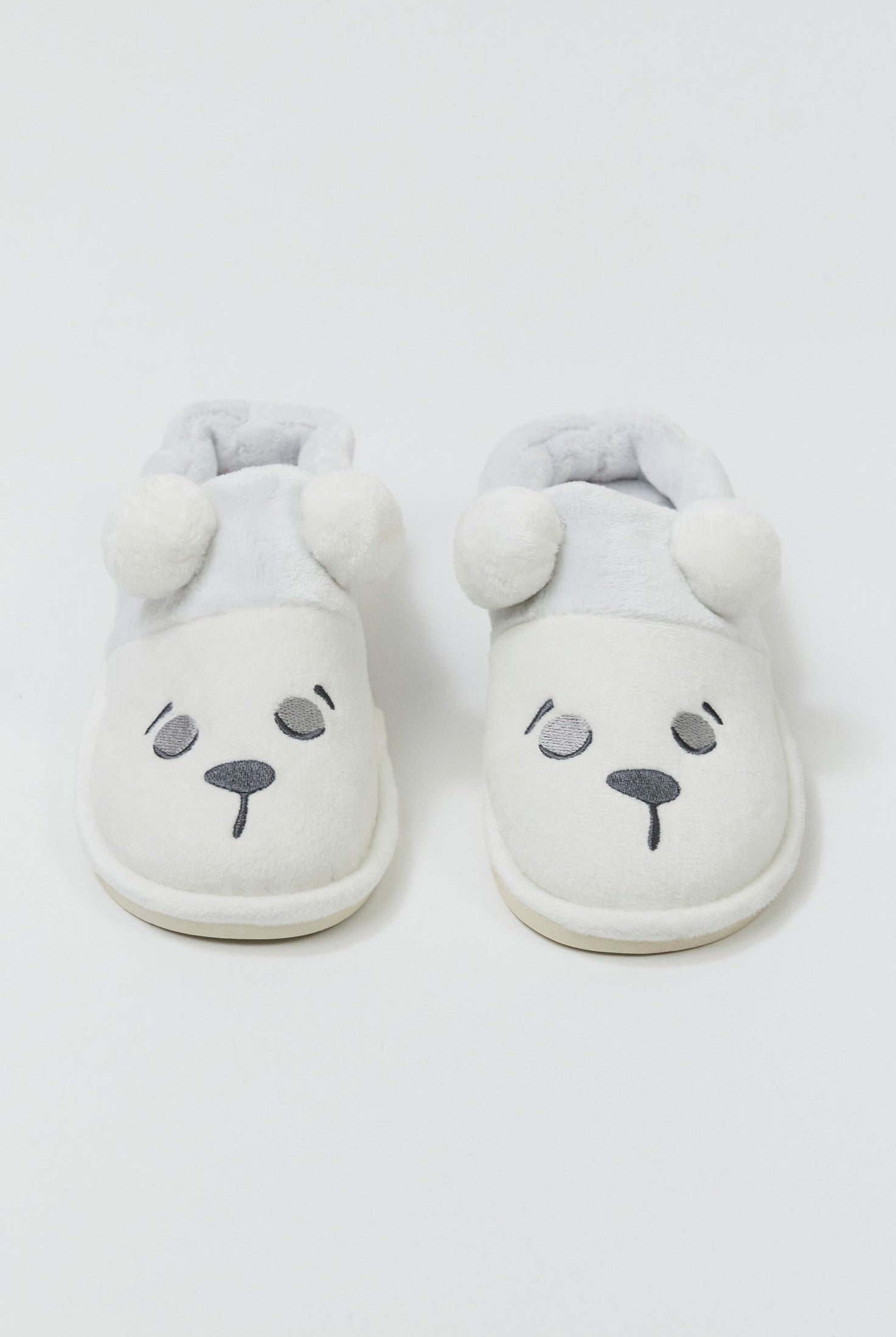 Pair of white slippers with bear face design on a light gray background