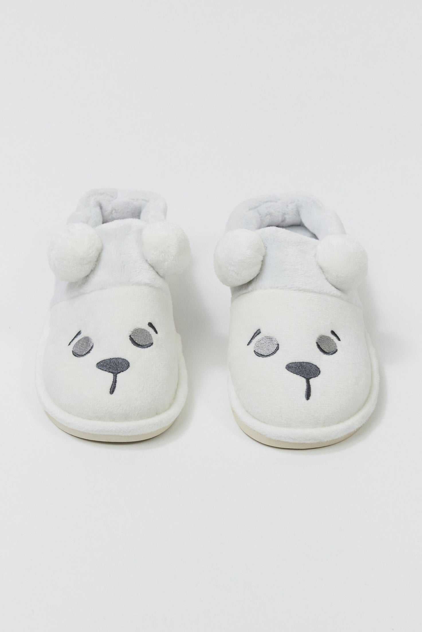 Pair of white slippers with bear face design on a light gray background