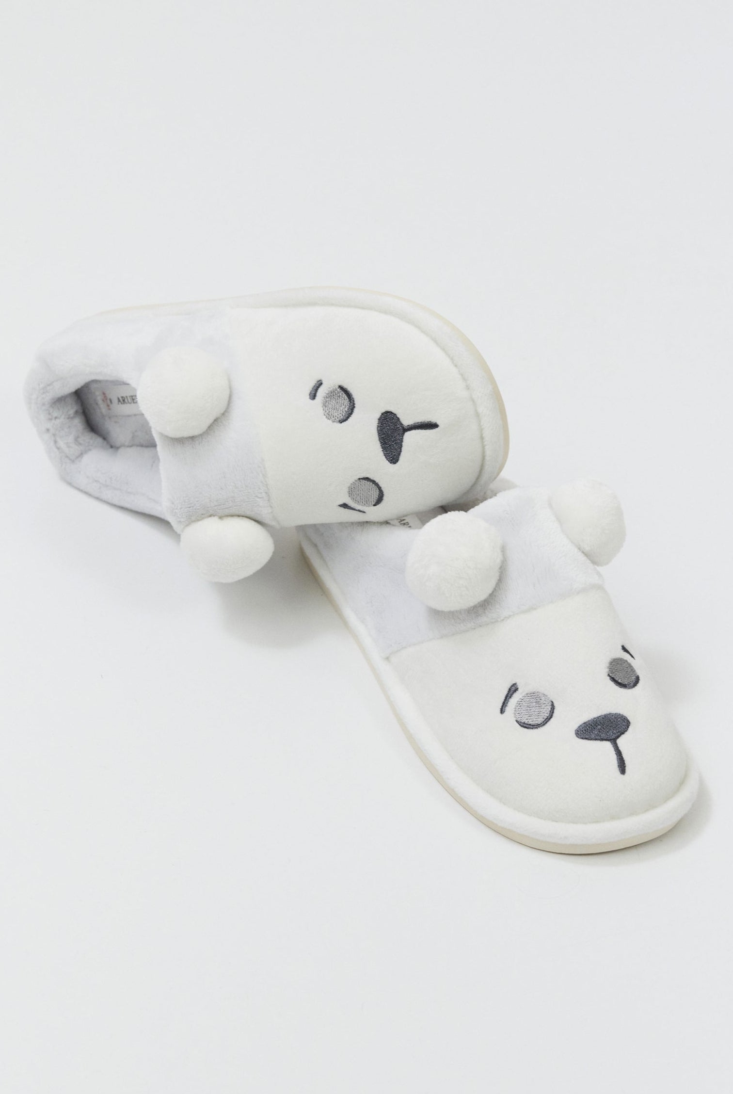 White plush slippers with bear face design on a light gray background