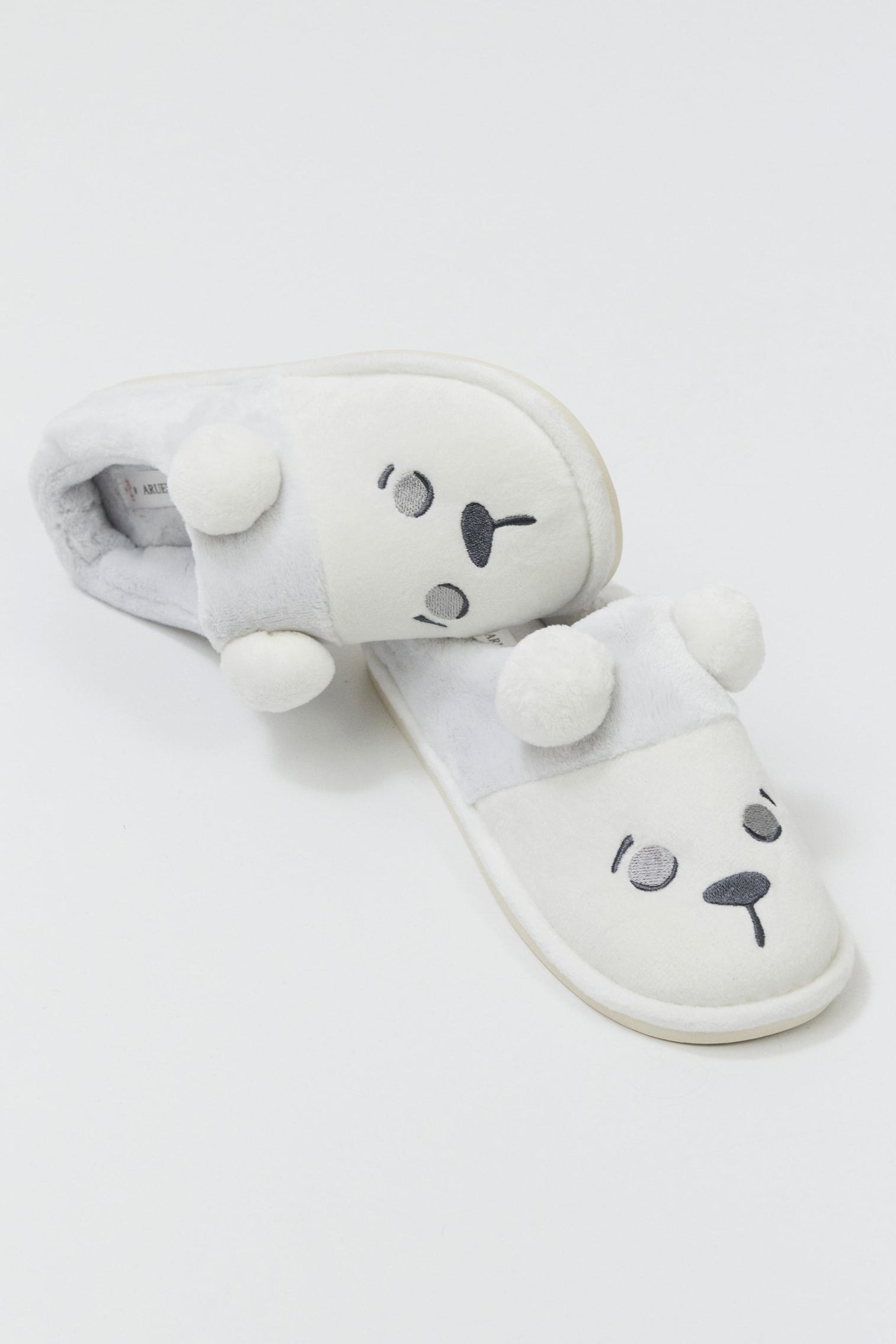 White plush slippers with bear face design on a light gray background