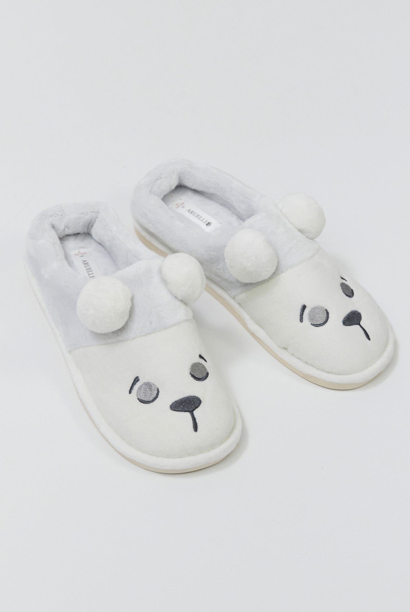 Pair of white slippers with bear face design on a light gray background