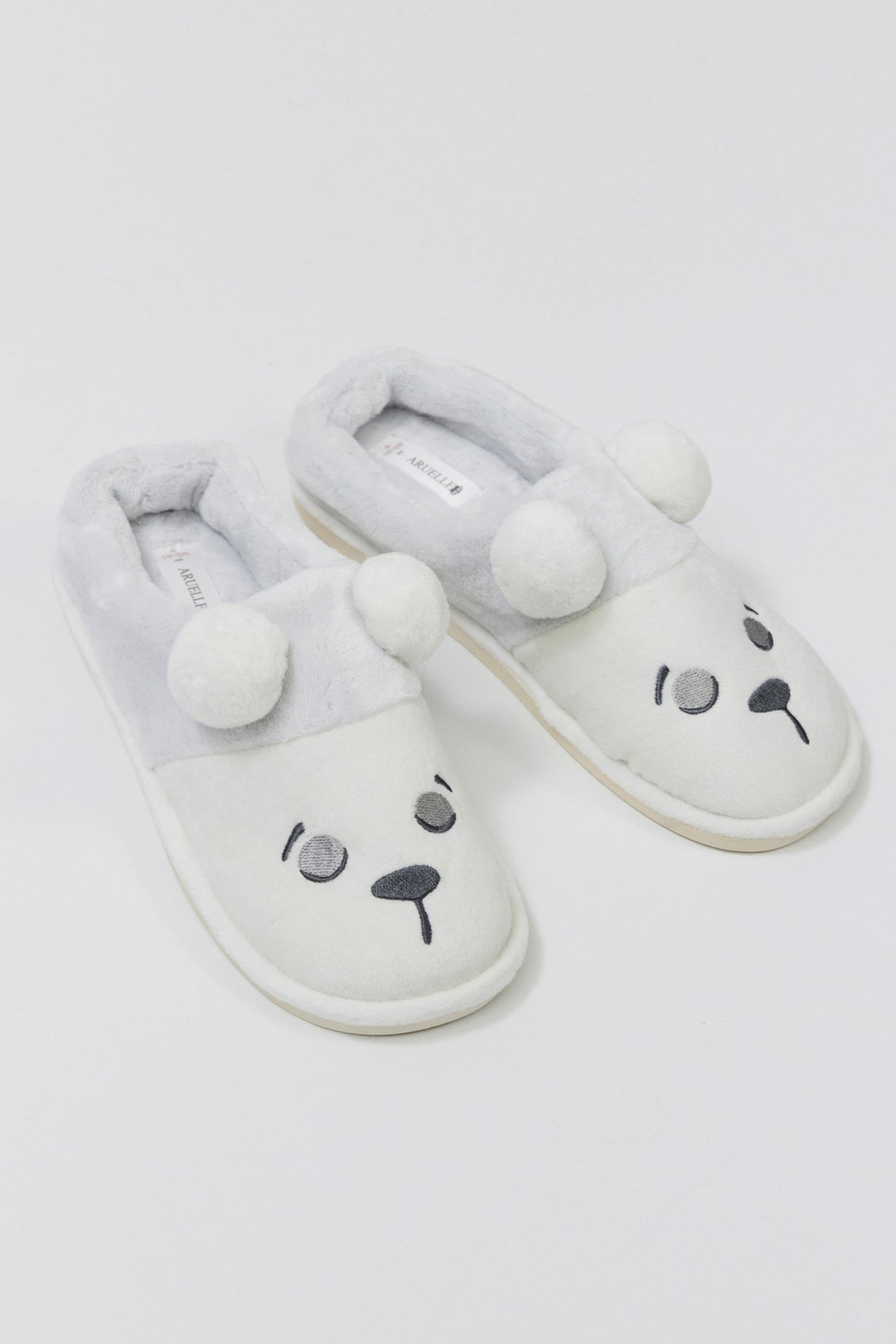 Pair of white slippers with bear face design on a light gray background
