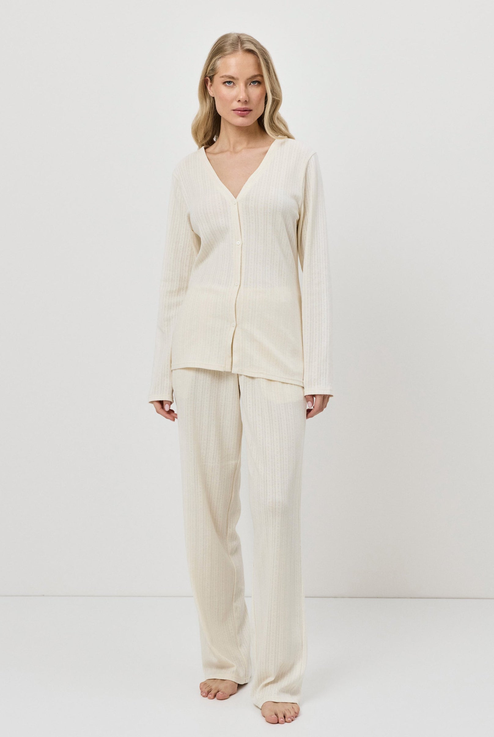 Woman wearing a cream-colored pajama set with pants against a white background