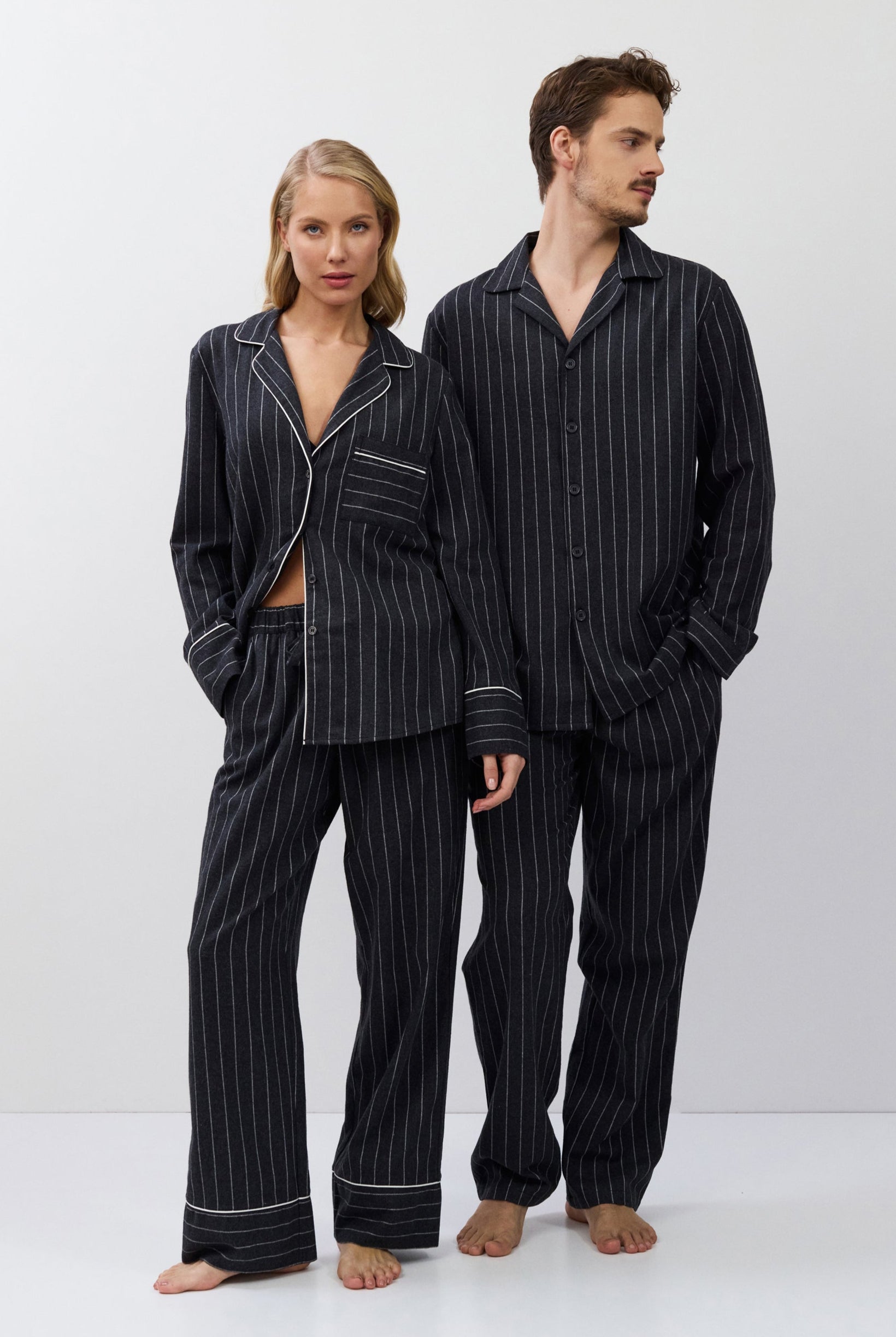 Two people wearing matching gray pinstripe pajamas on a white background
