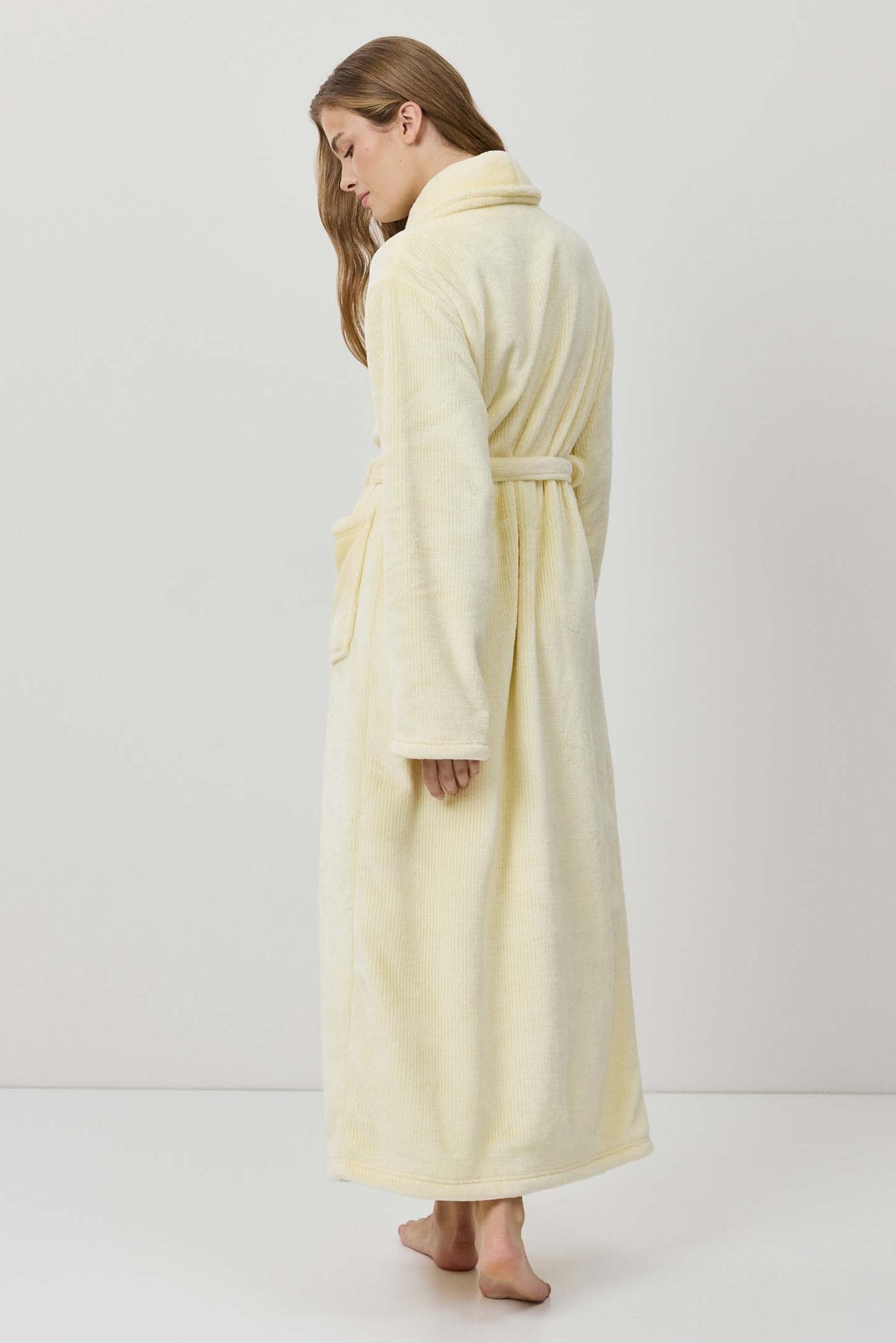 Woman wearing a long cream-colored robe against a white background