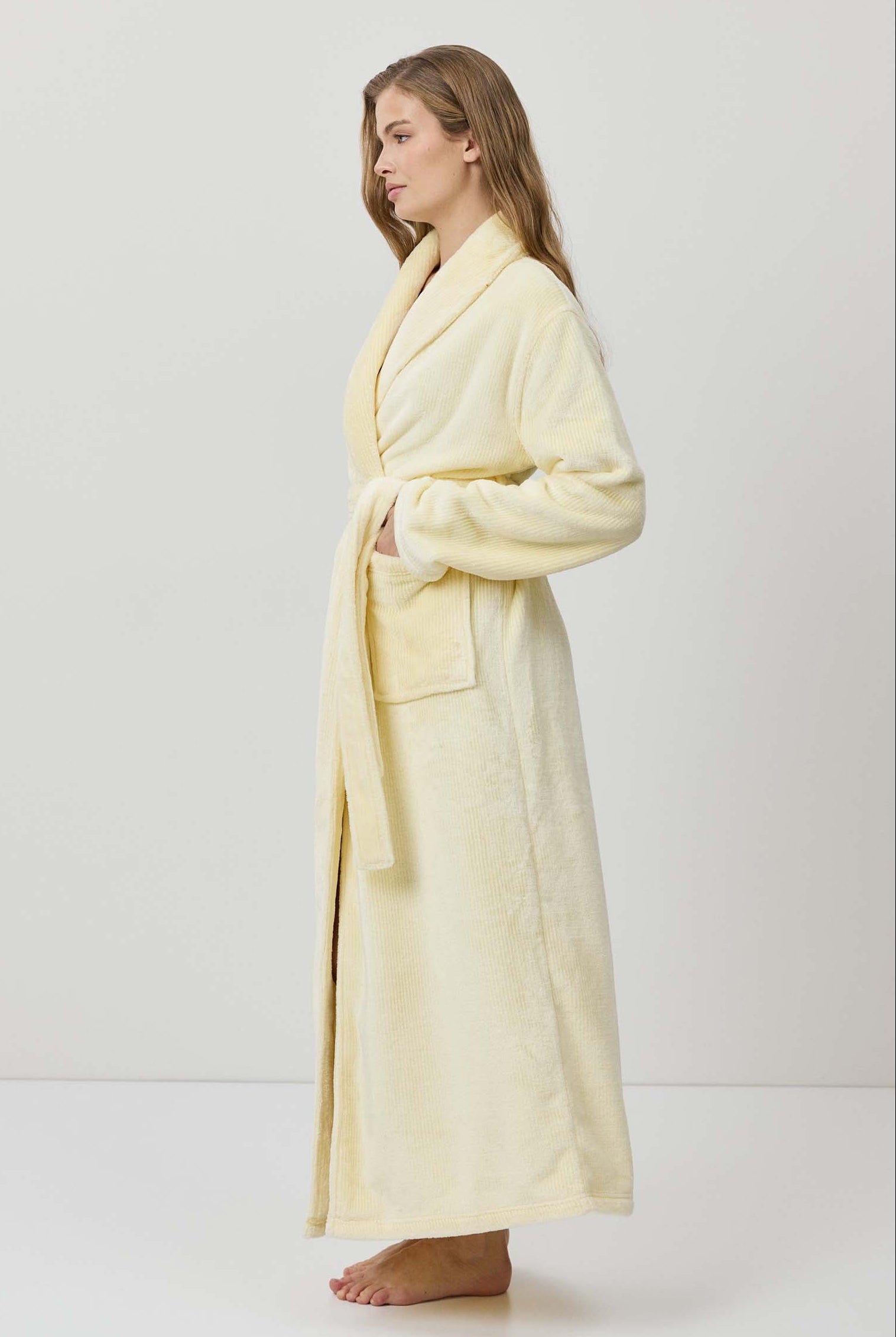 Woman wearing a light yellow bathrobe against a white background