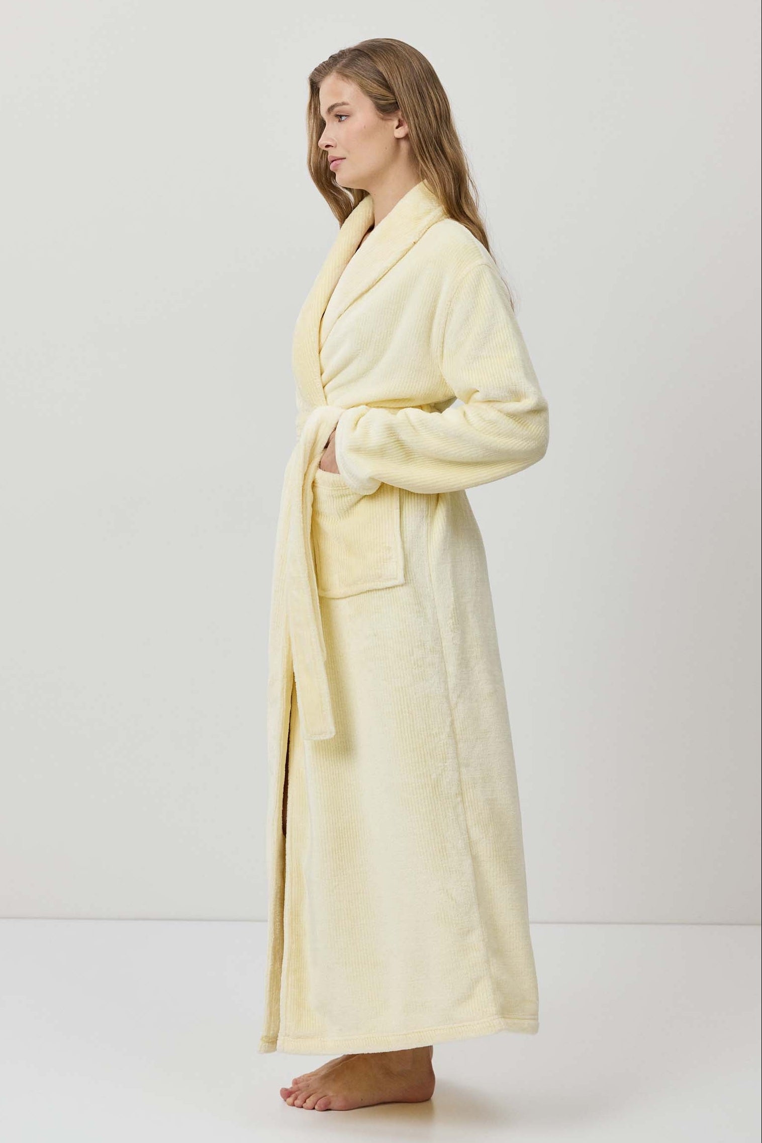 Woman wearing a light yellow bathrobe against a white background