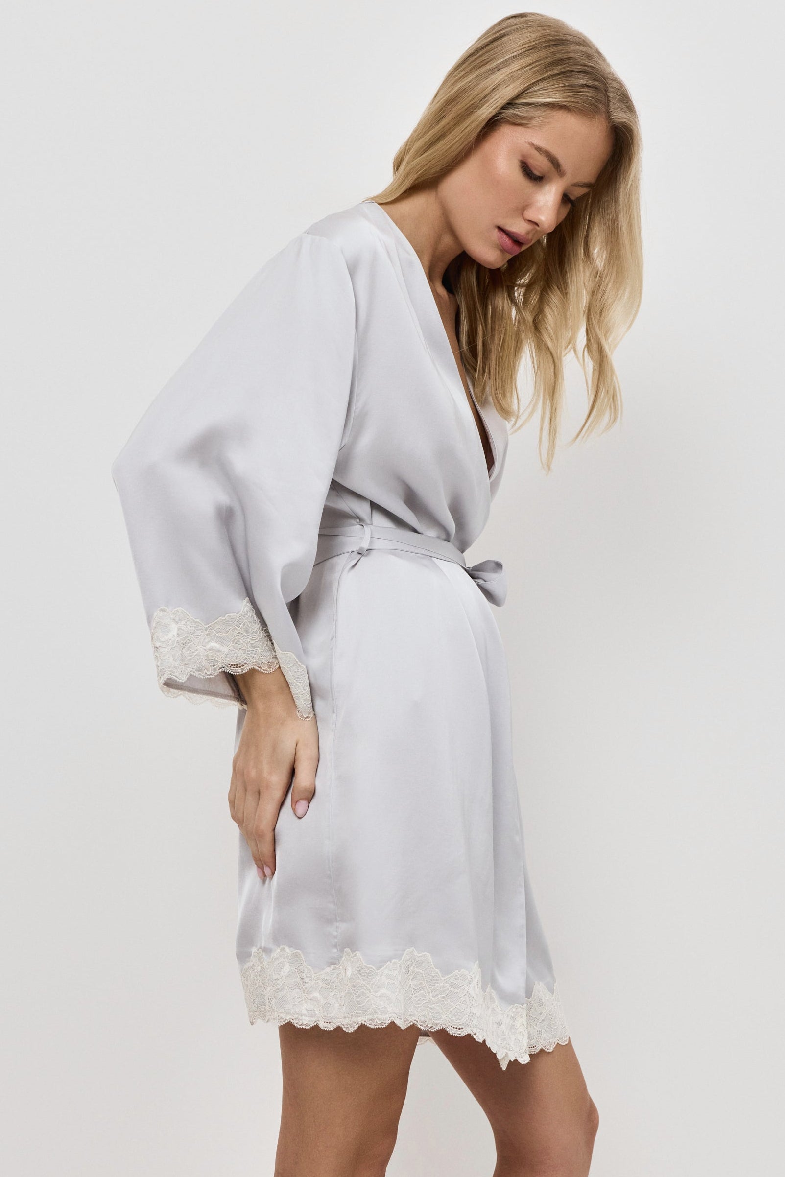 Woman wearing a gray satin robe with lace trim on a plain background