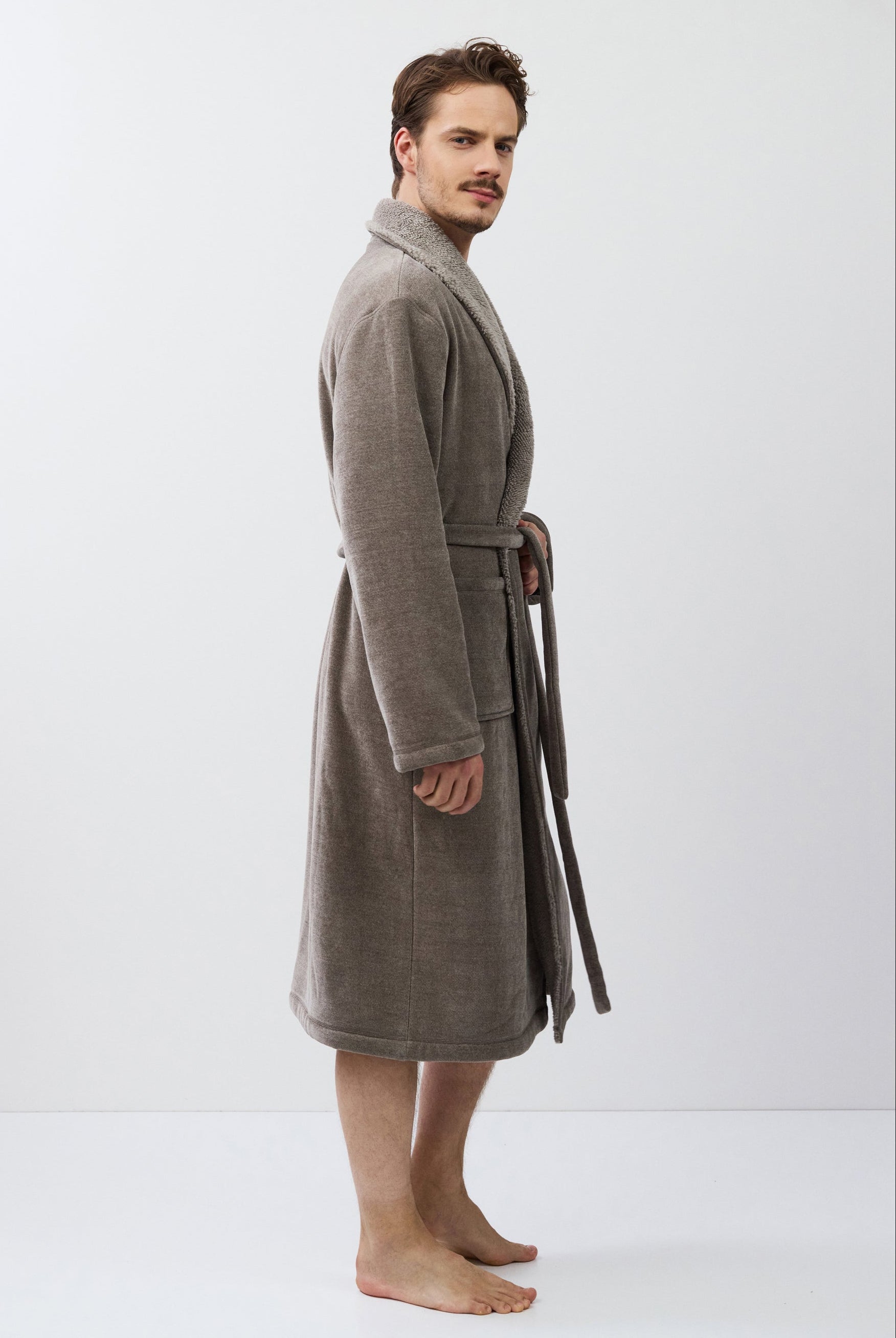 Man wearing a brown bathrobe standing against a white background