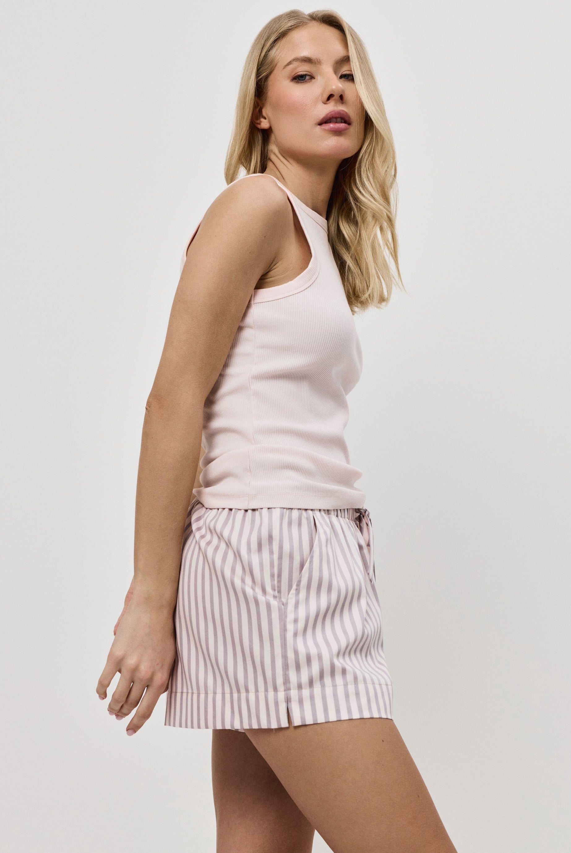 Woman wearing a light pink sleeveless top and striped pajama shorts on a white background