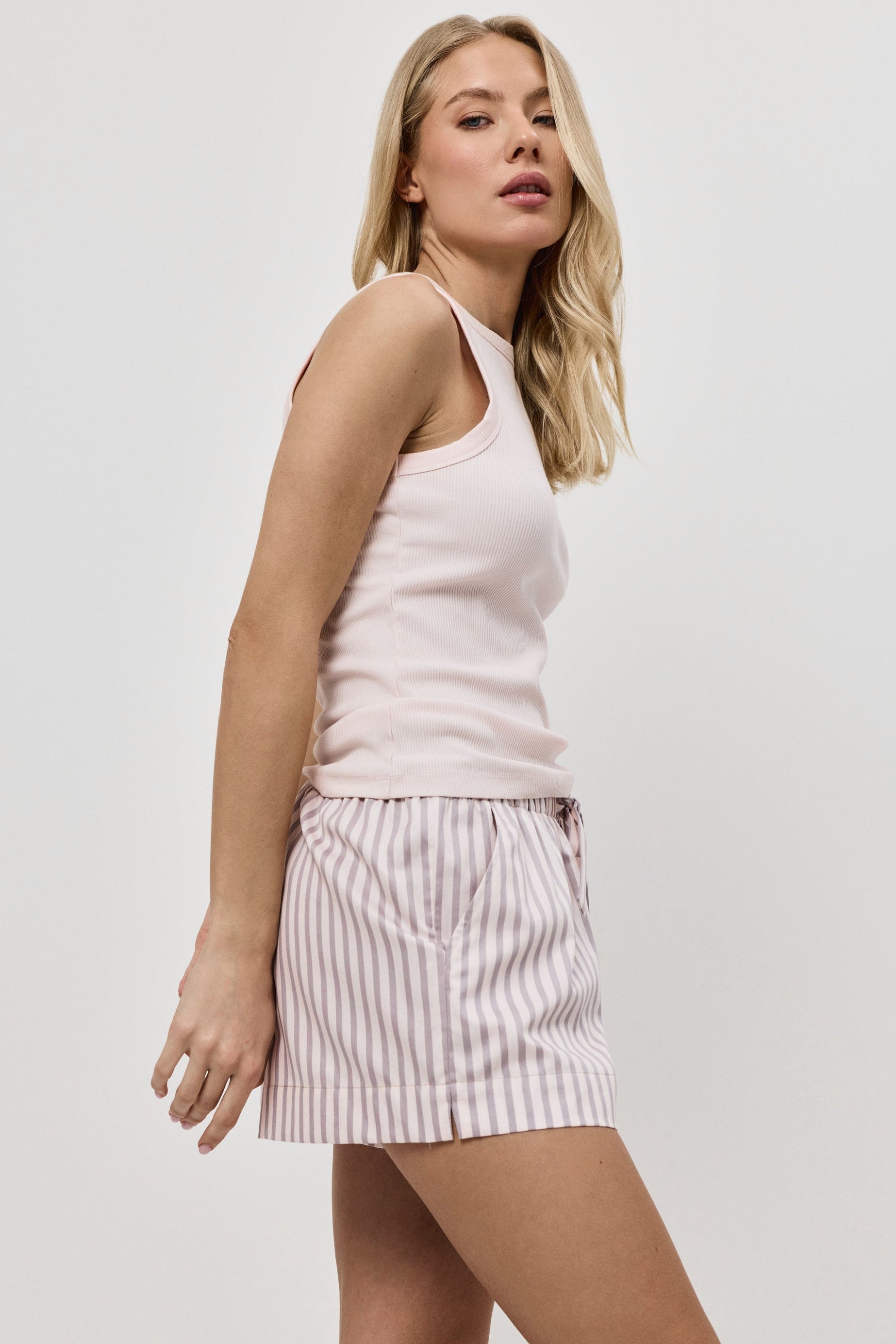 Woman wearing a light pink sleeveless top and striped pajama shorts on a white background