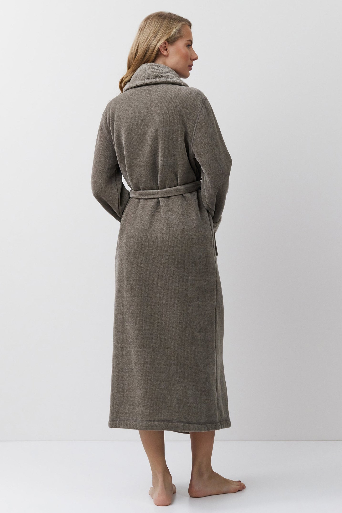 Woman wearing a brown bathrobe standing against a white background