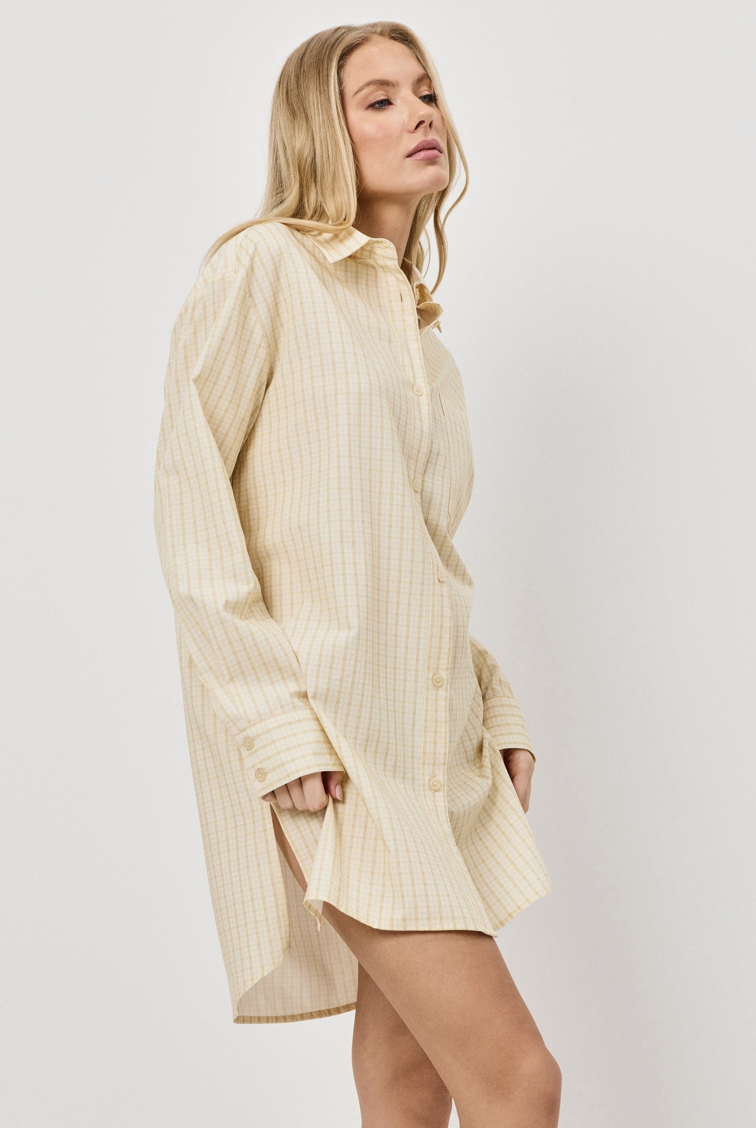 Woman wearing a long yellow shirt nightdress against a white background