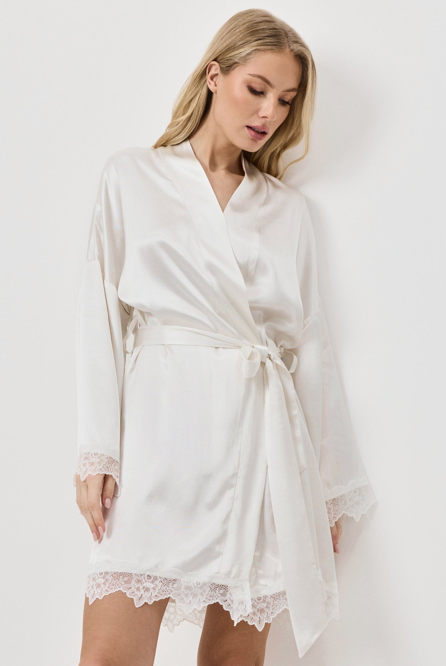 Woman wearing a white gown with lace hem on a plain background