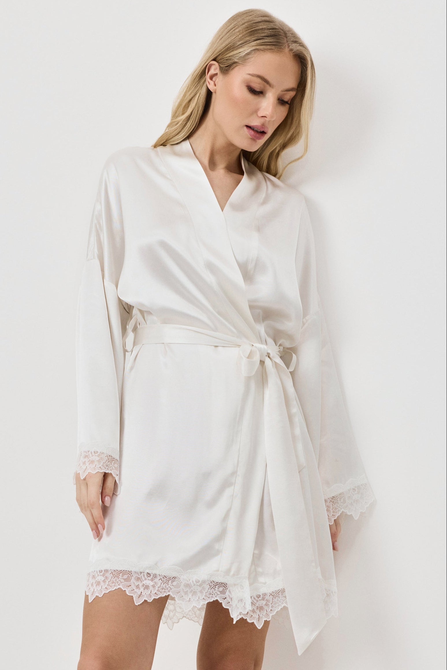 Woman wearing a white gown with lace hem on a plain background