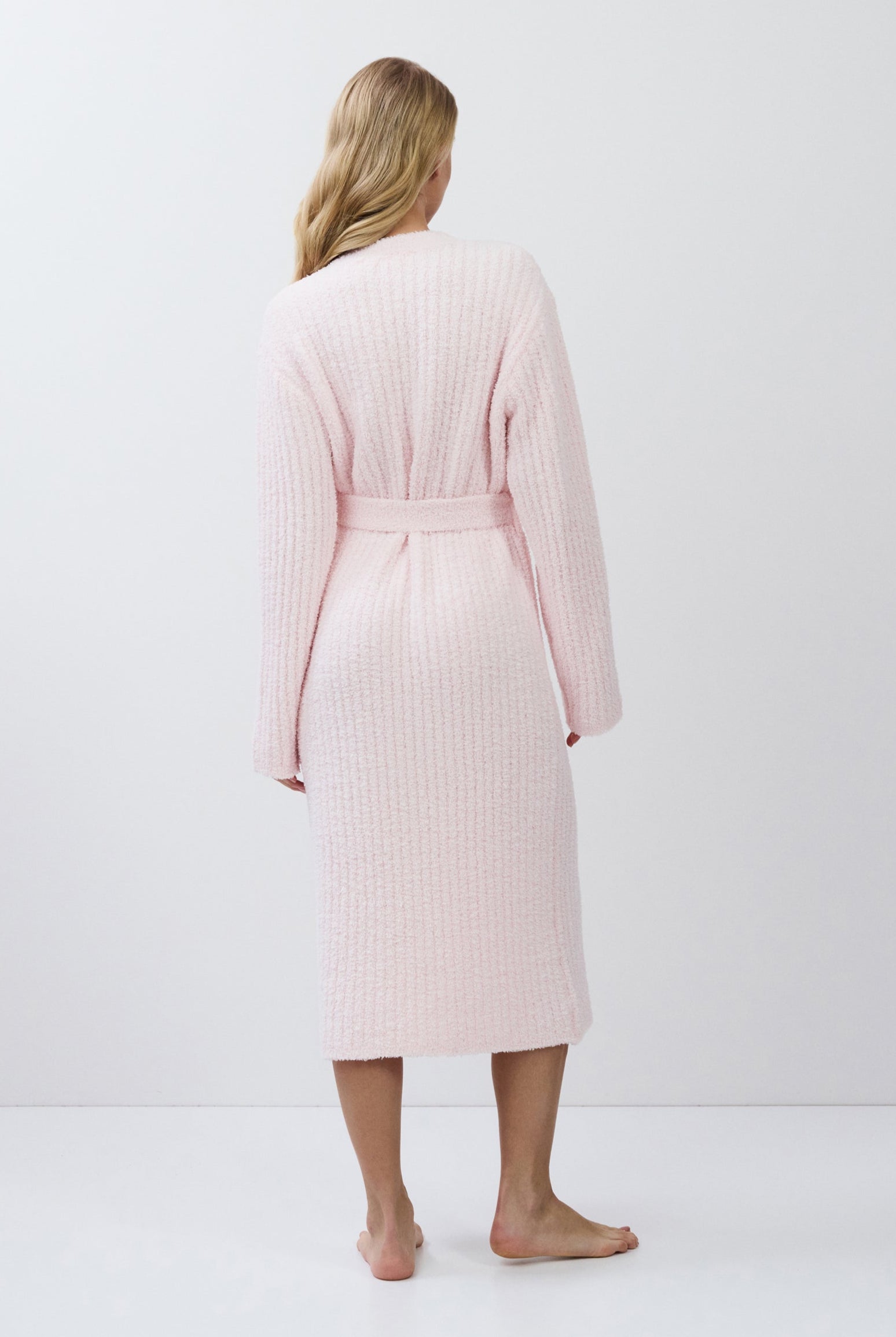 Woman wearing a light pink ribbed bathrobe against a white background