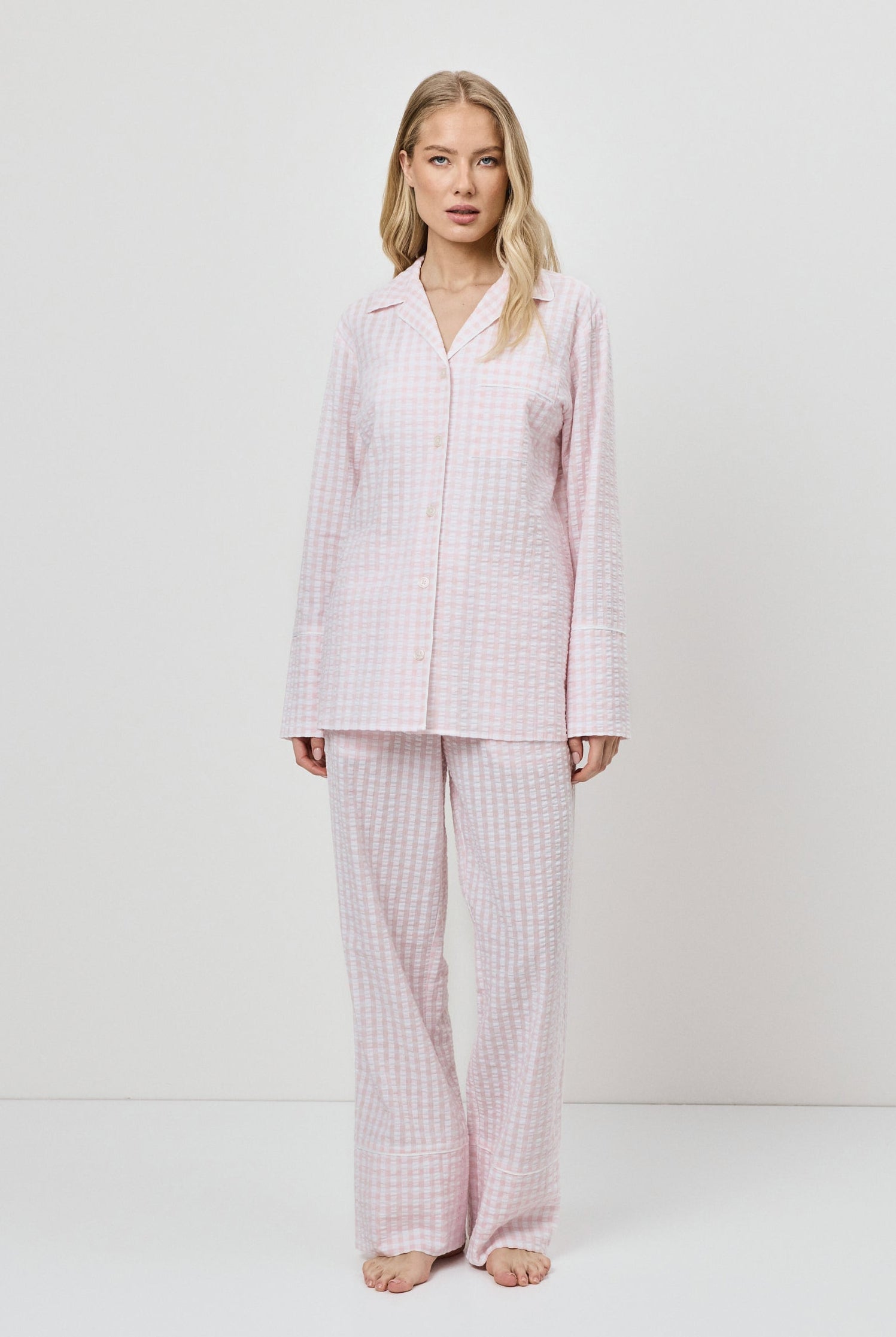 Woman wearing a pink checkered pajama set against a white background