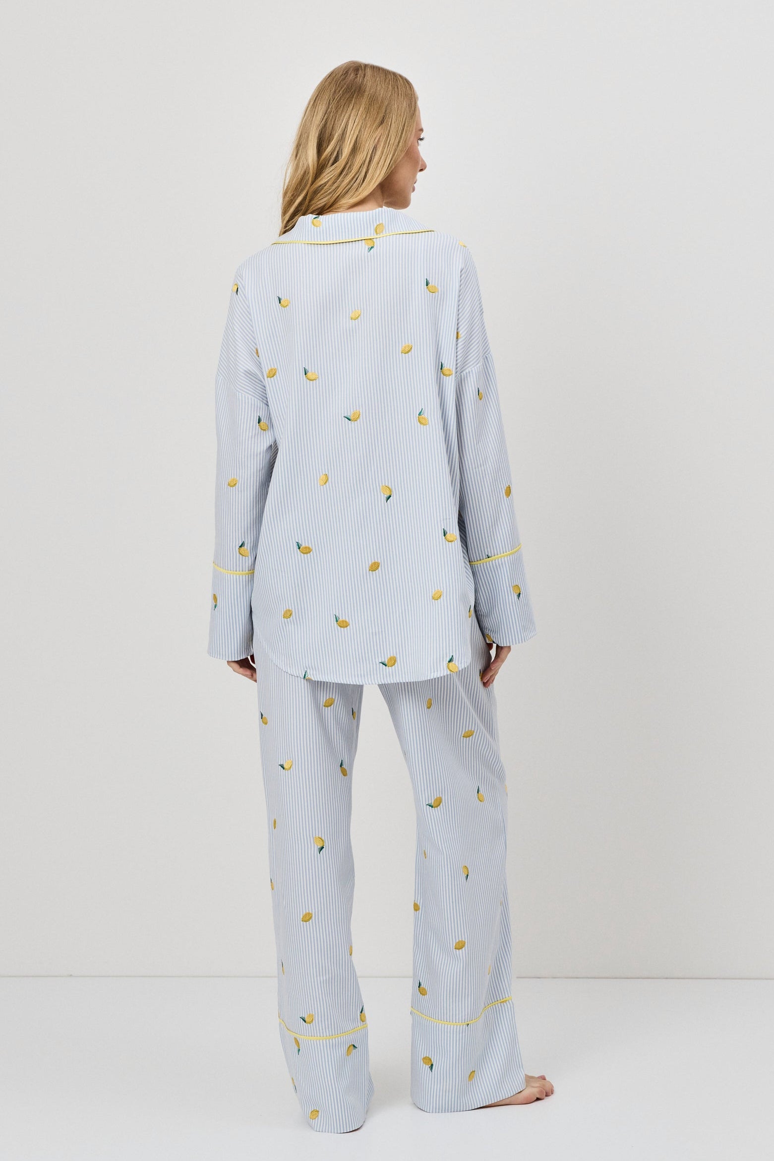 Woman wearing light blue pajama set with small lemons embroideries on a white background