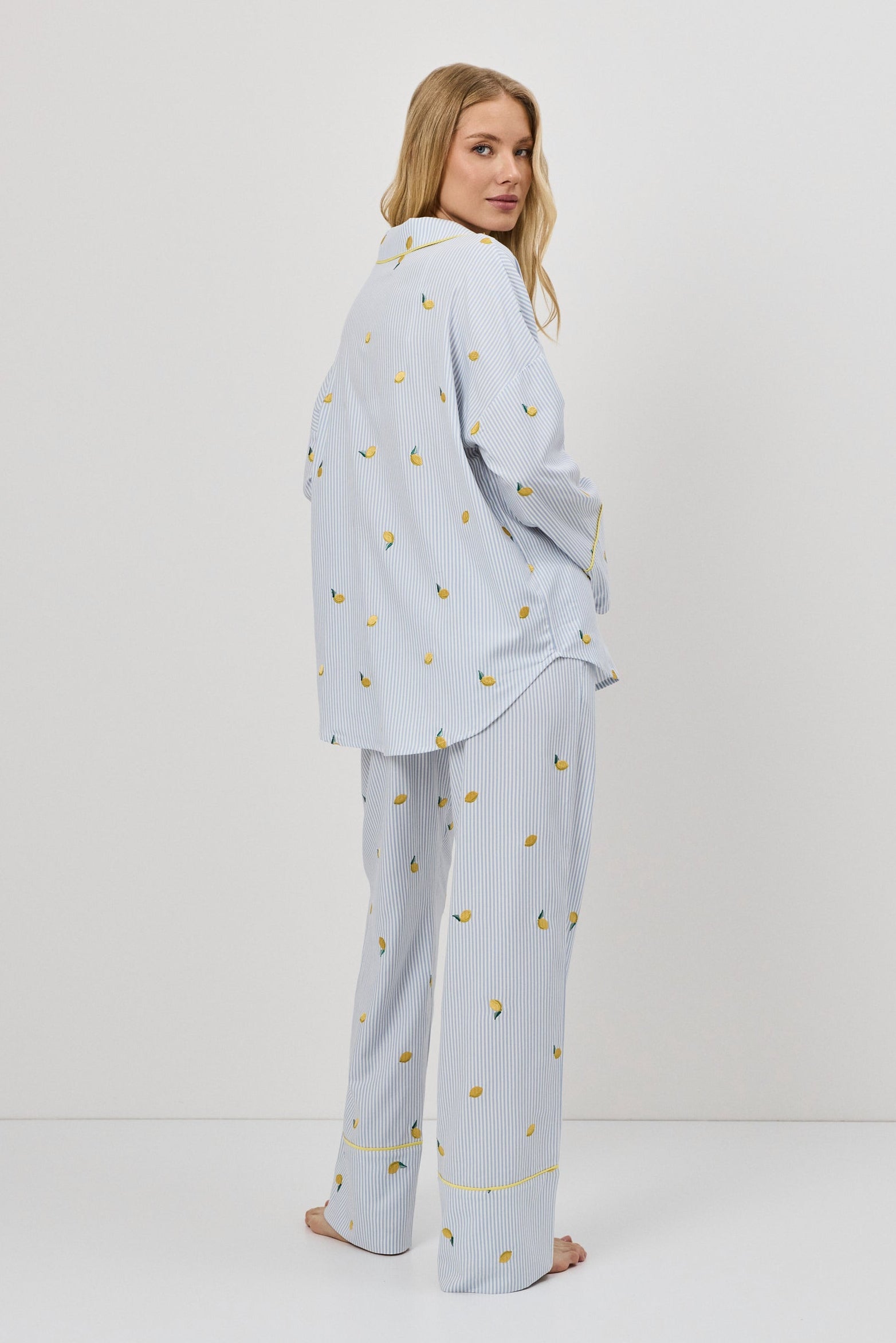 Woman wearing a light blue pajama set with a lemon emroyderies on a white background