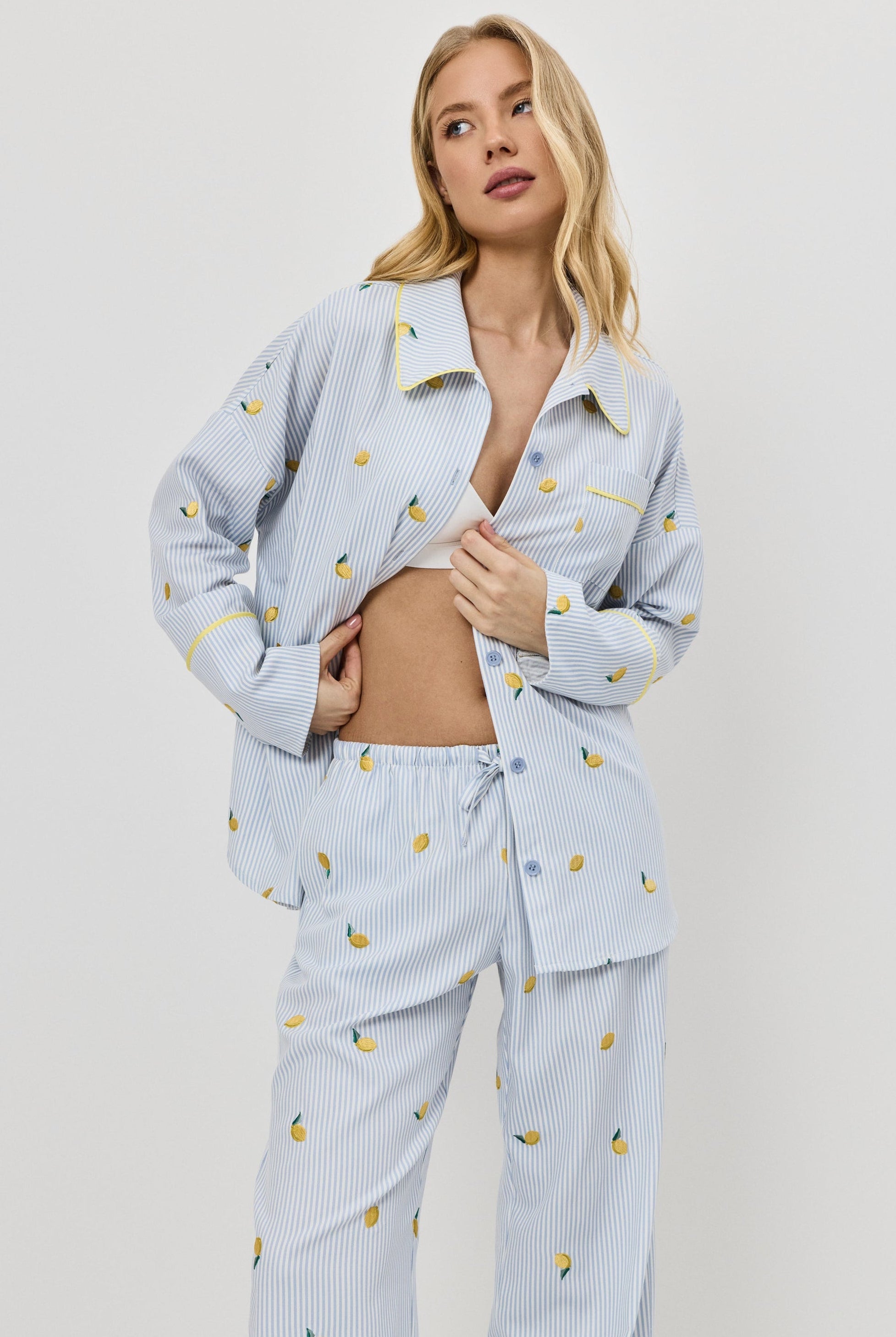 Woman wearing a light blue pajama set with lemon embroideries on a plain background