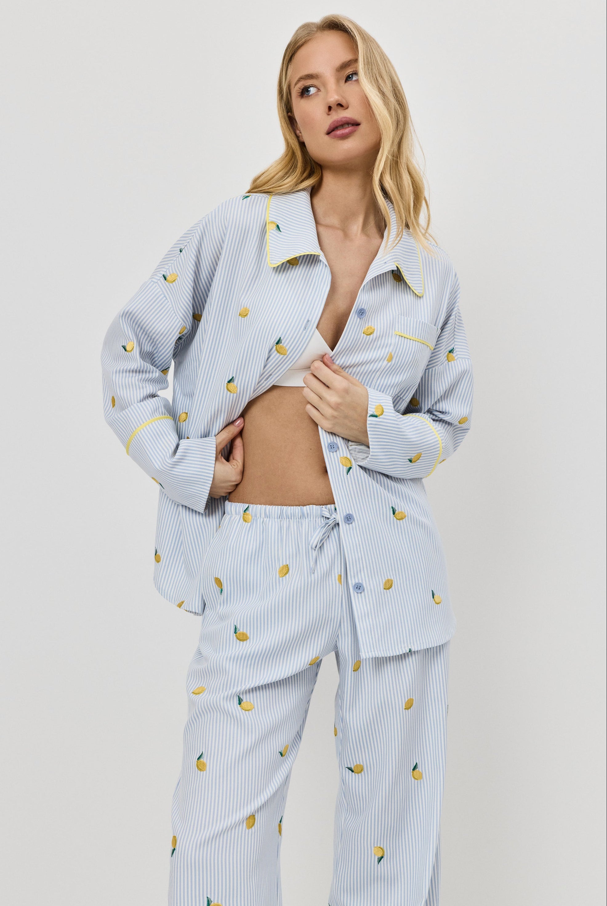 Woman wearing a light blue pajama set with lemon embroideries on a plain background