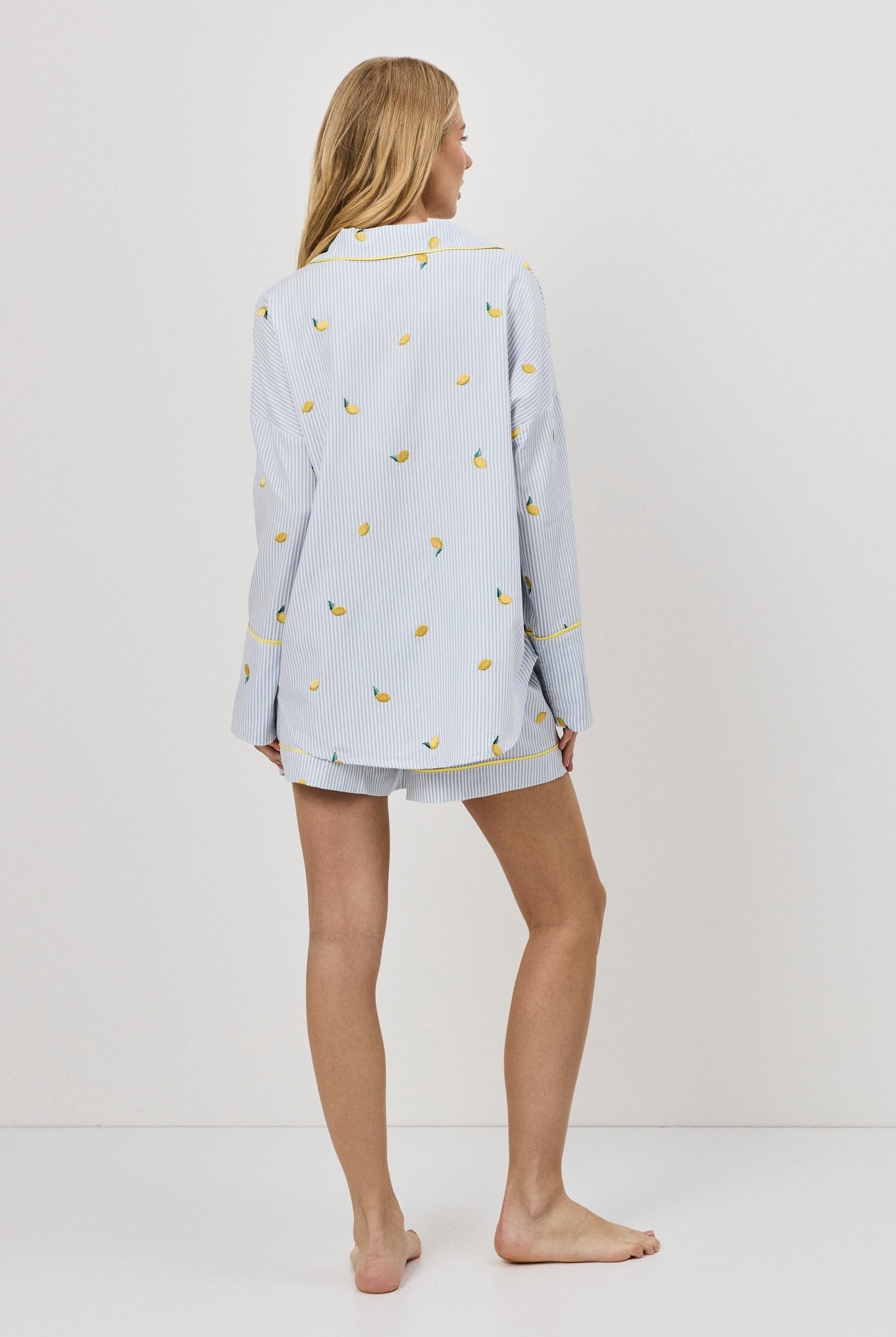 Woman wearing a light blue pajama set with lemon embroideries on a white background
