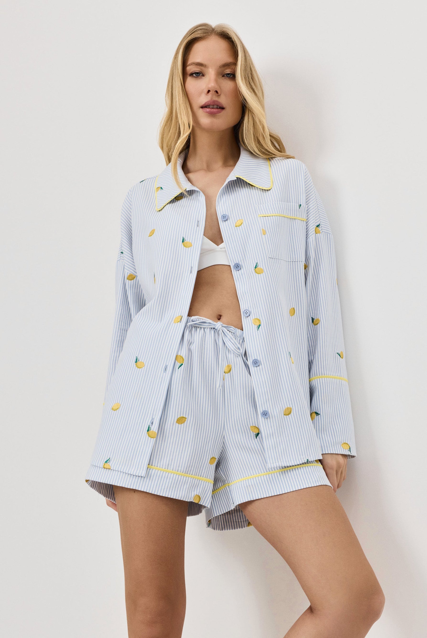 Woman wearing a light blue pajama set with lemon emroideries on a white background