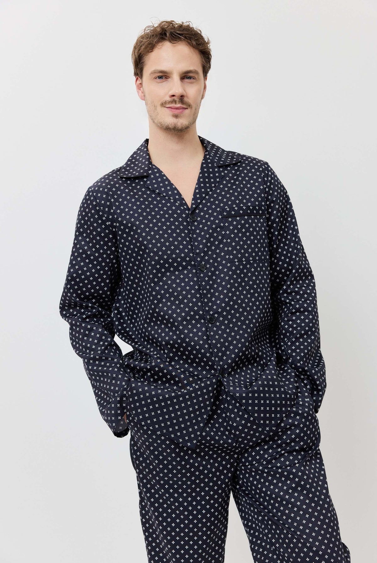 Man wearing a navy blue polka dot shirt and pants on a light gray background
