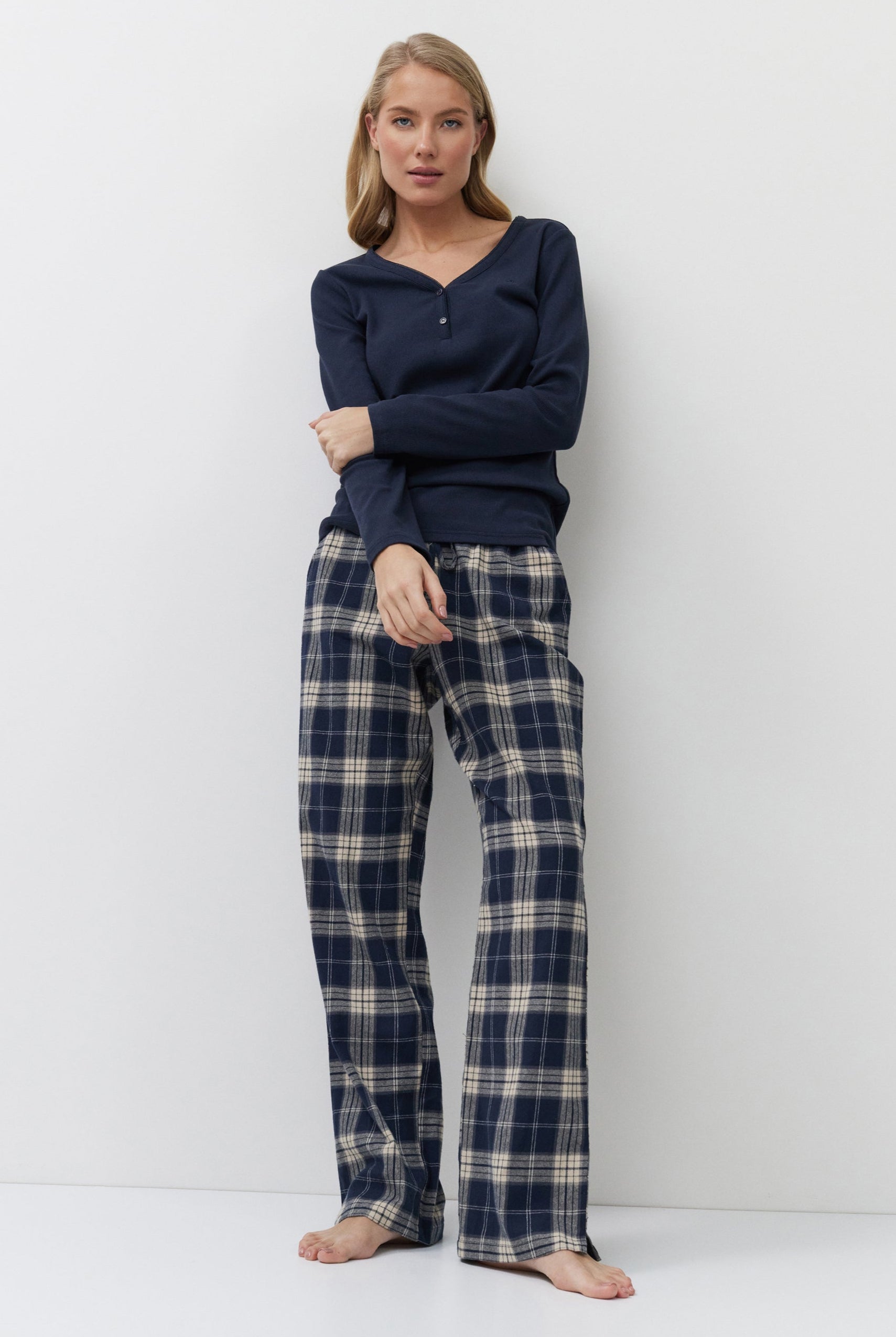 Woman wearing navy long-sleeve top and plaid pants against a white background