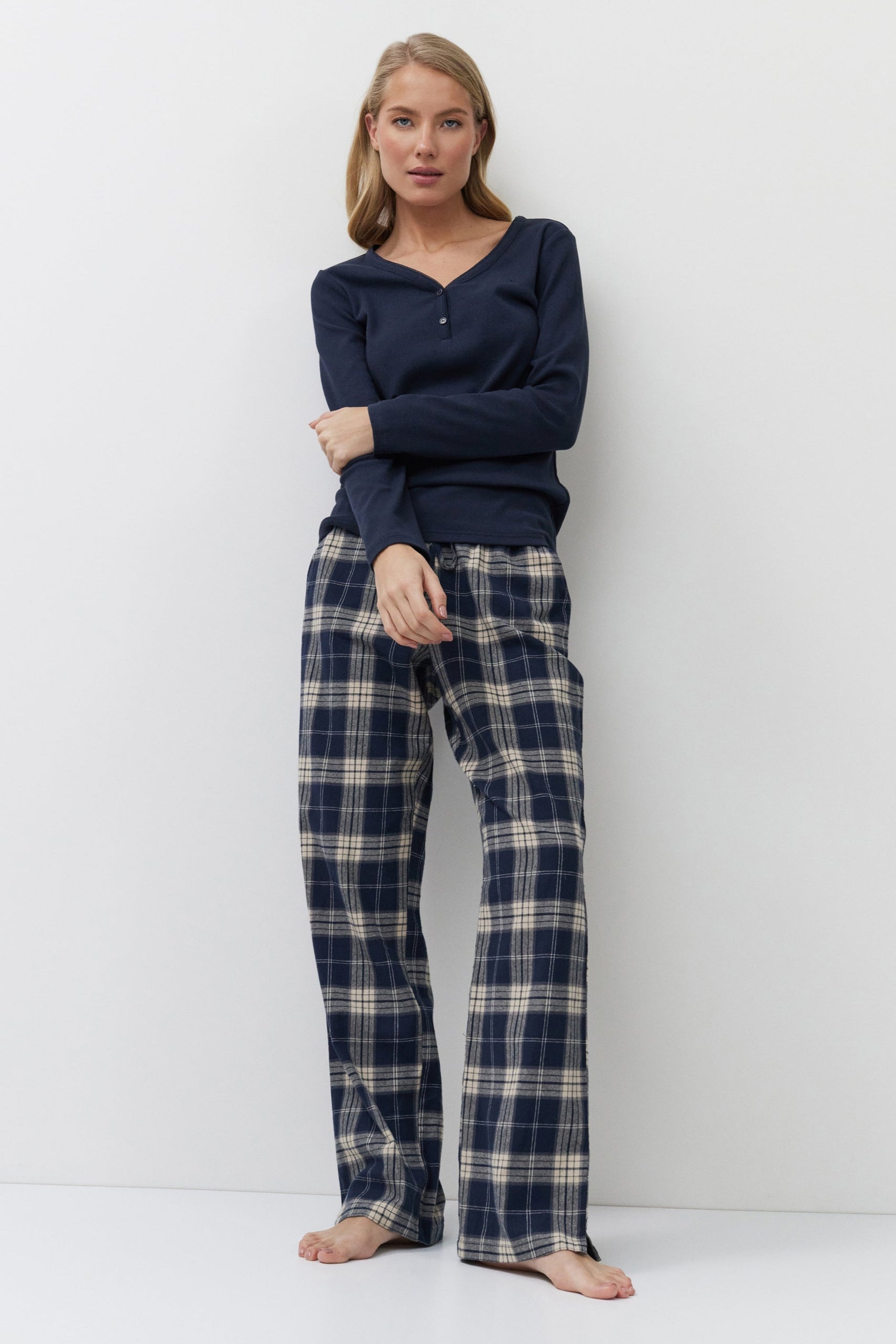 Woman wearing navy long-sleeve top and plaid pants against a white background