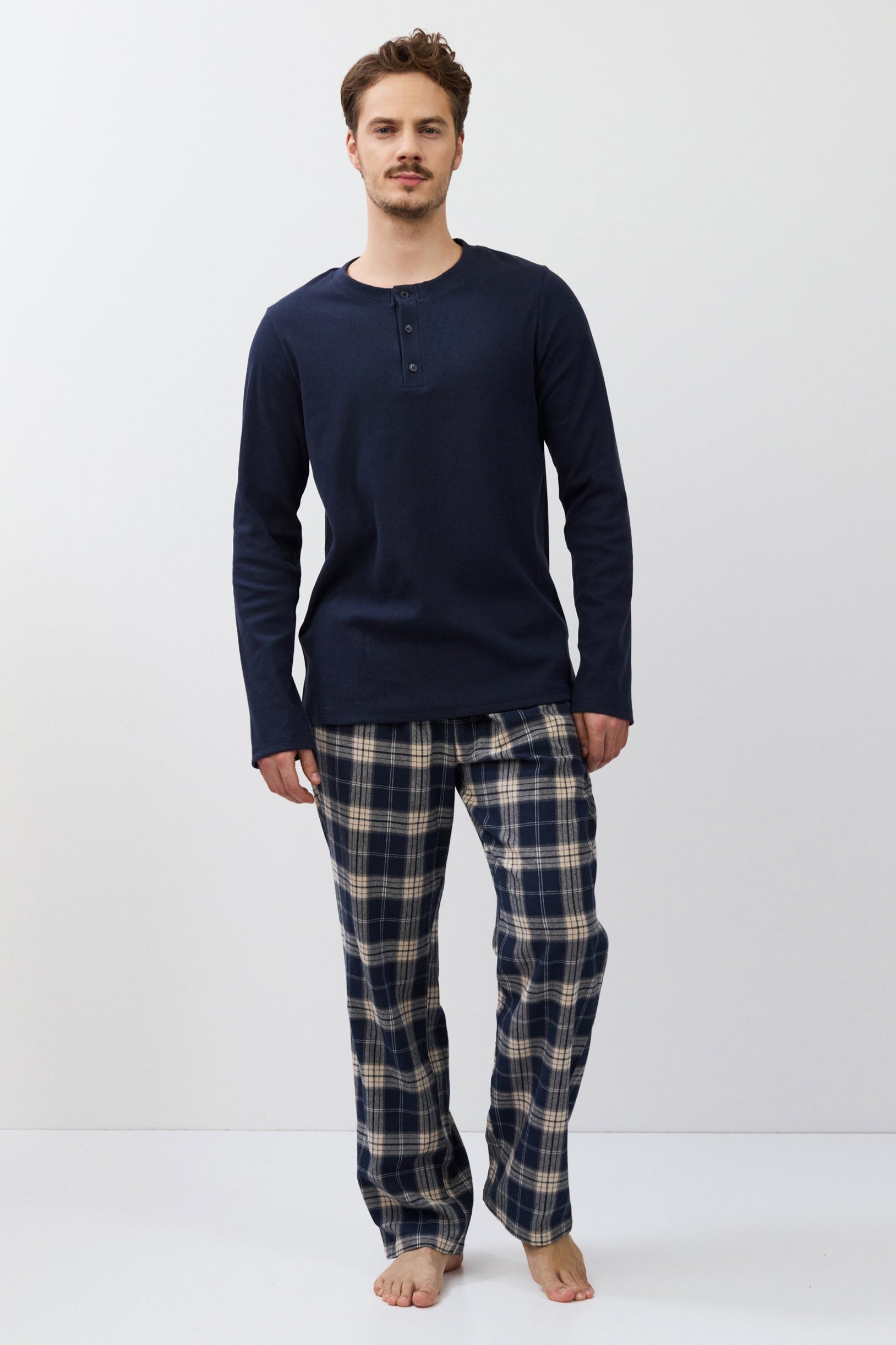 Man wearing a navy long-sleeve shirt and plaid pants on a white background