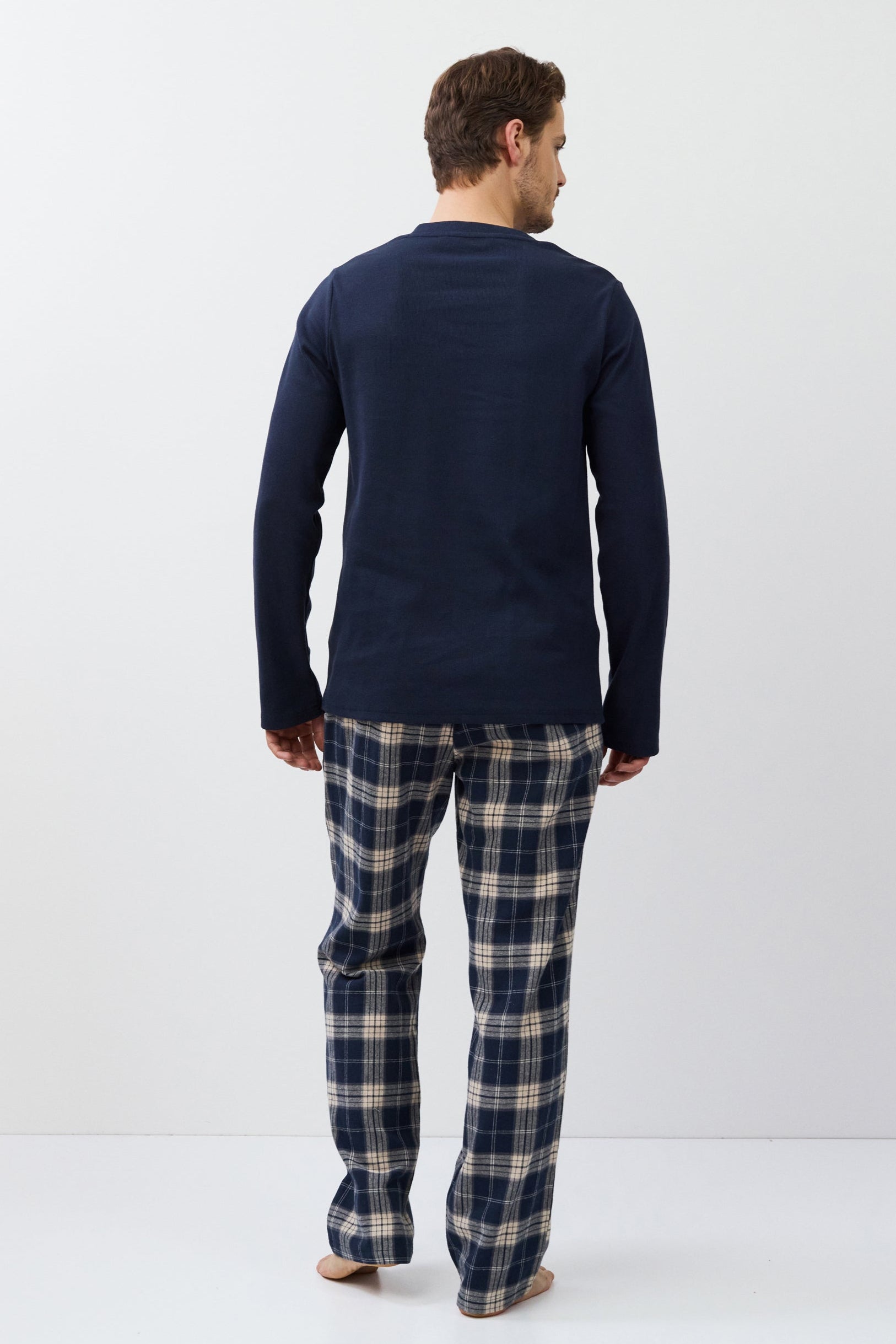 Man wearing navy long-sleeve top and plaid pants on a white background