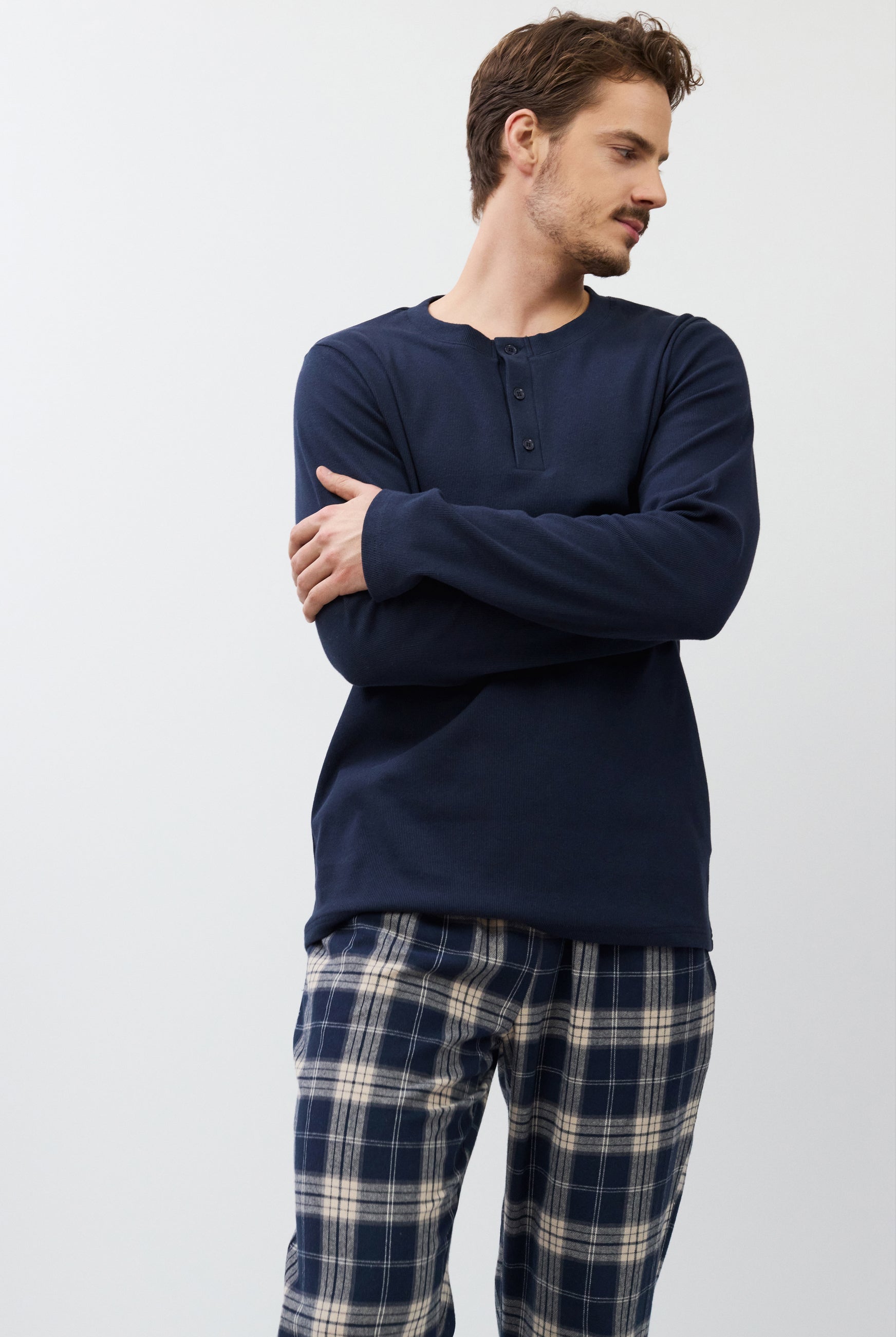 Man wearing a navy long-sleeve shirt and plaid pants against a white background