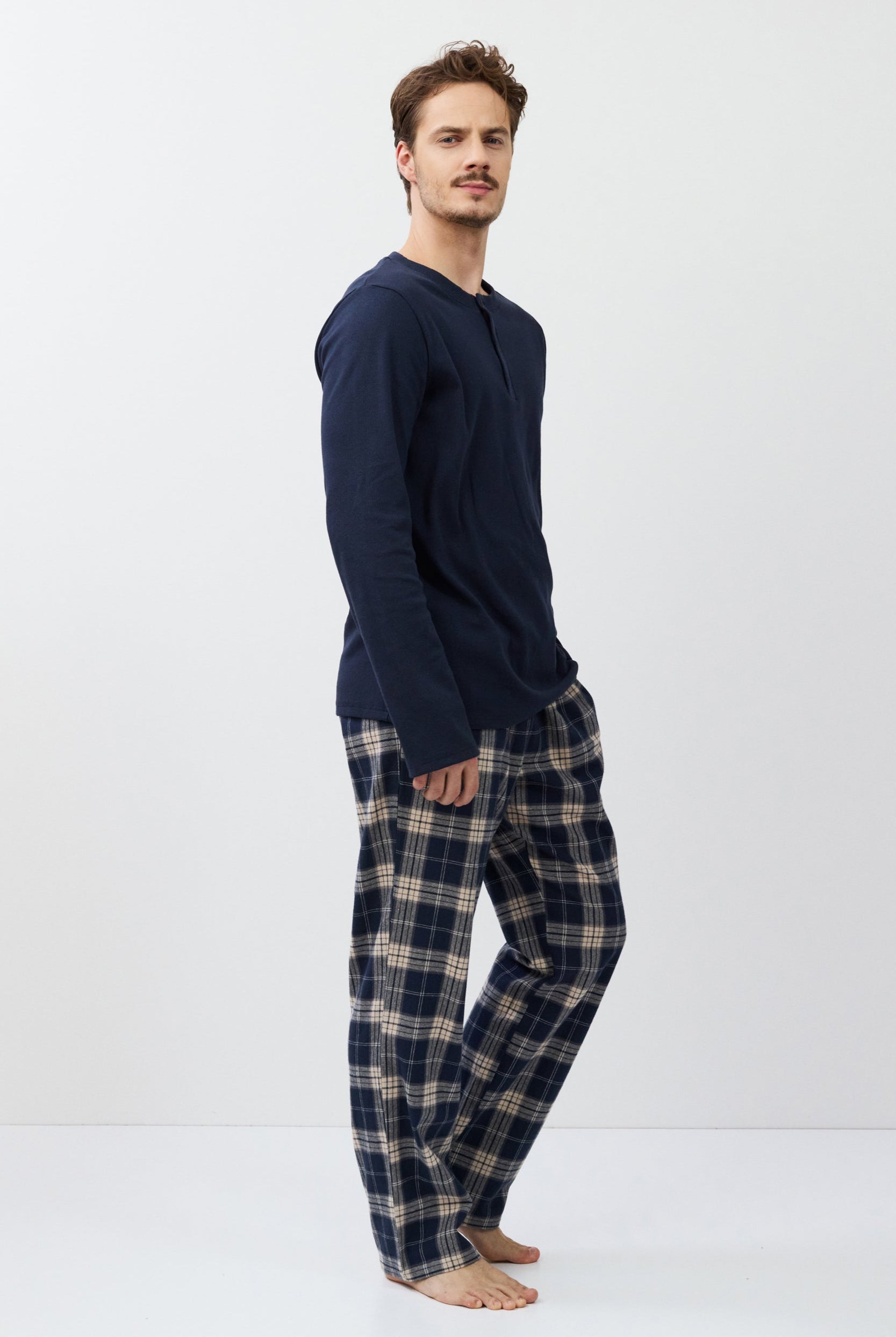 Man wearing navy long-sleeve top and plaid pants on a white background