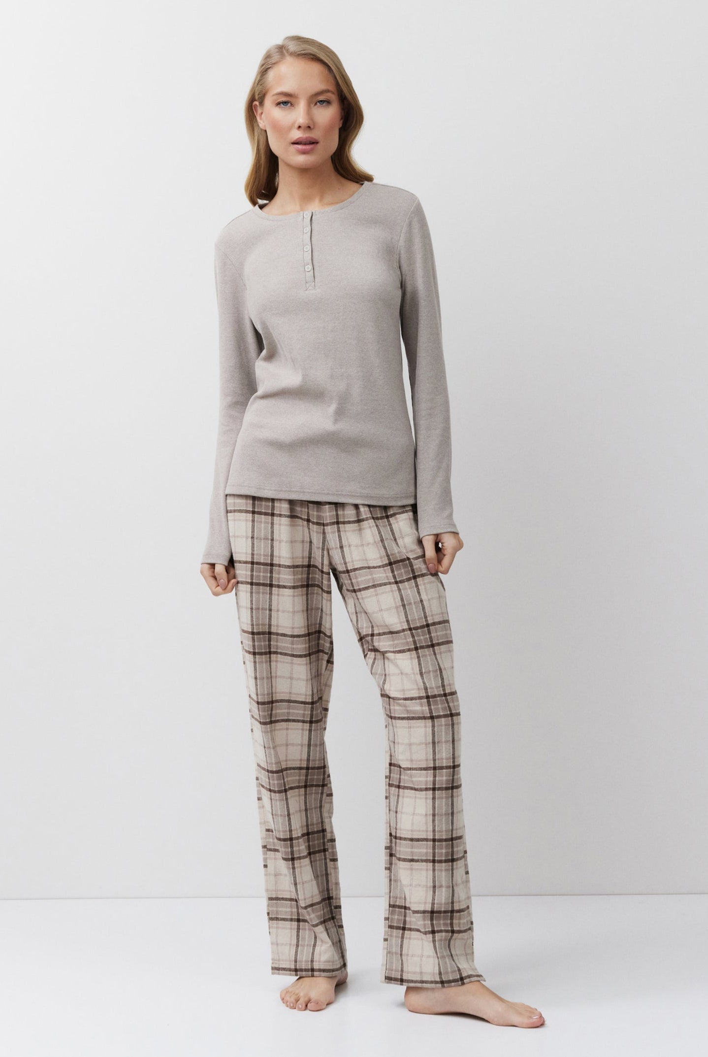 Woman wearing a beige long-sleeve top and plaid pants on a white background