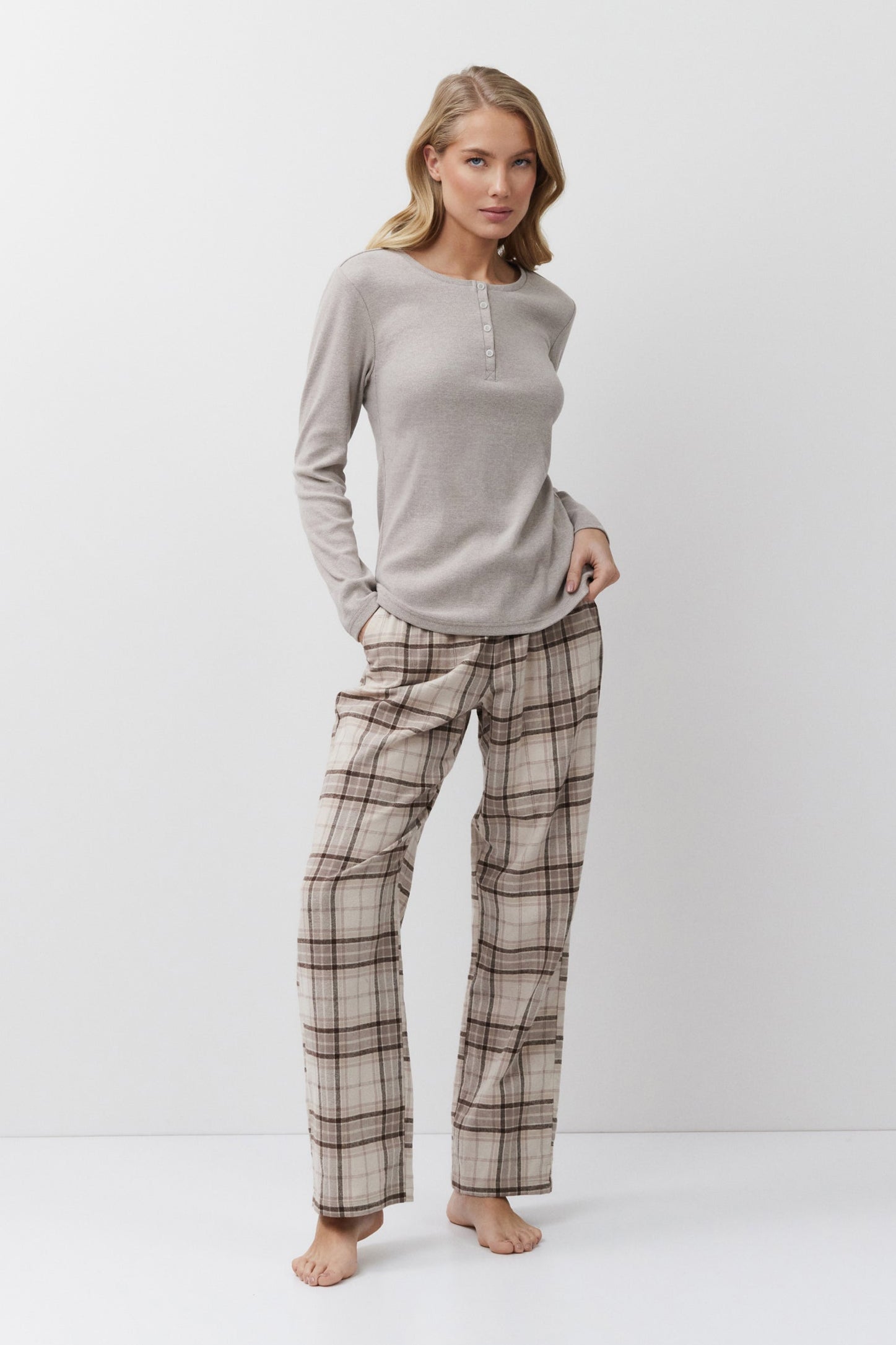 Woman wearing a beige long-sleeve top and plaid pants on a white background