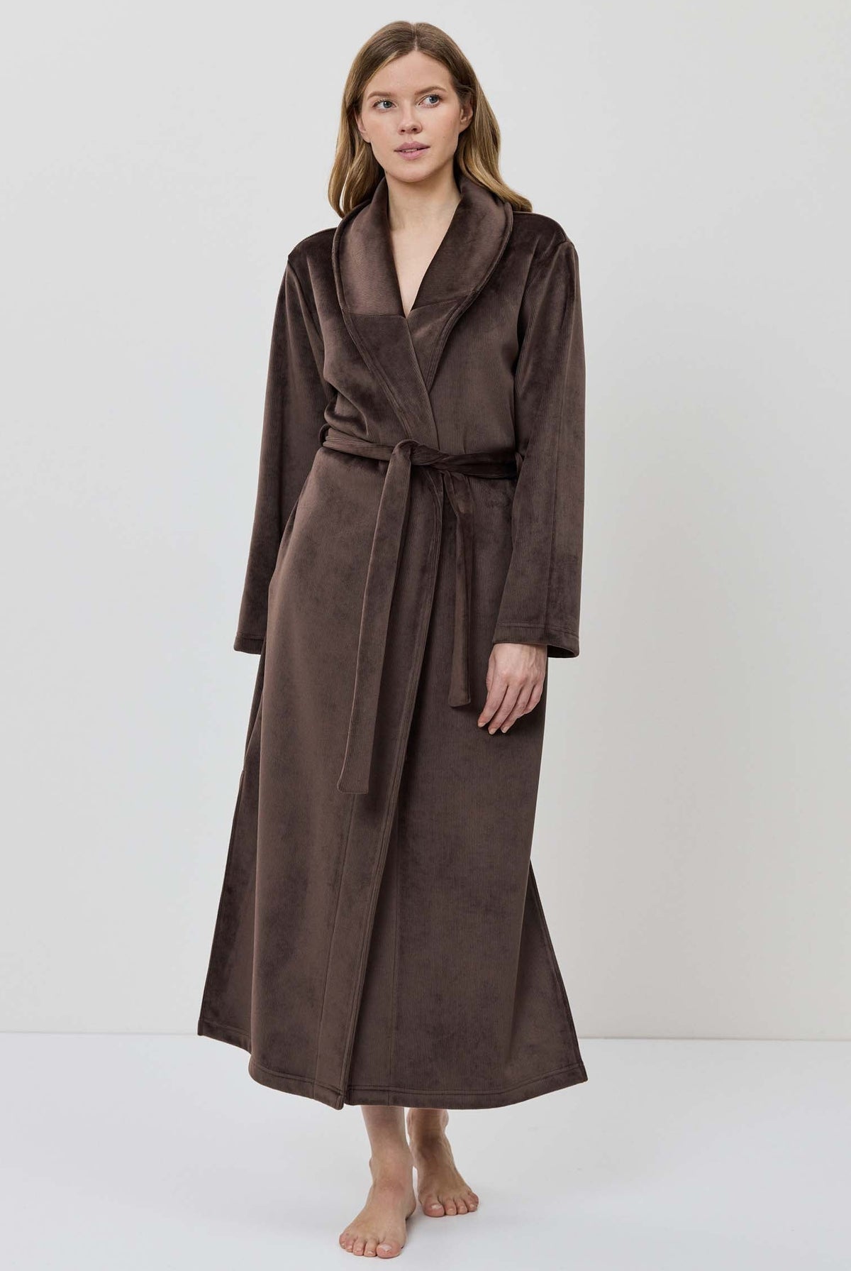 A woman wearing a long brown plush bathrobe with a tie belt.