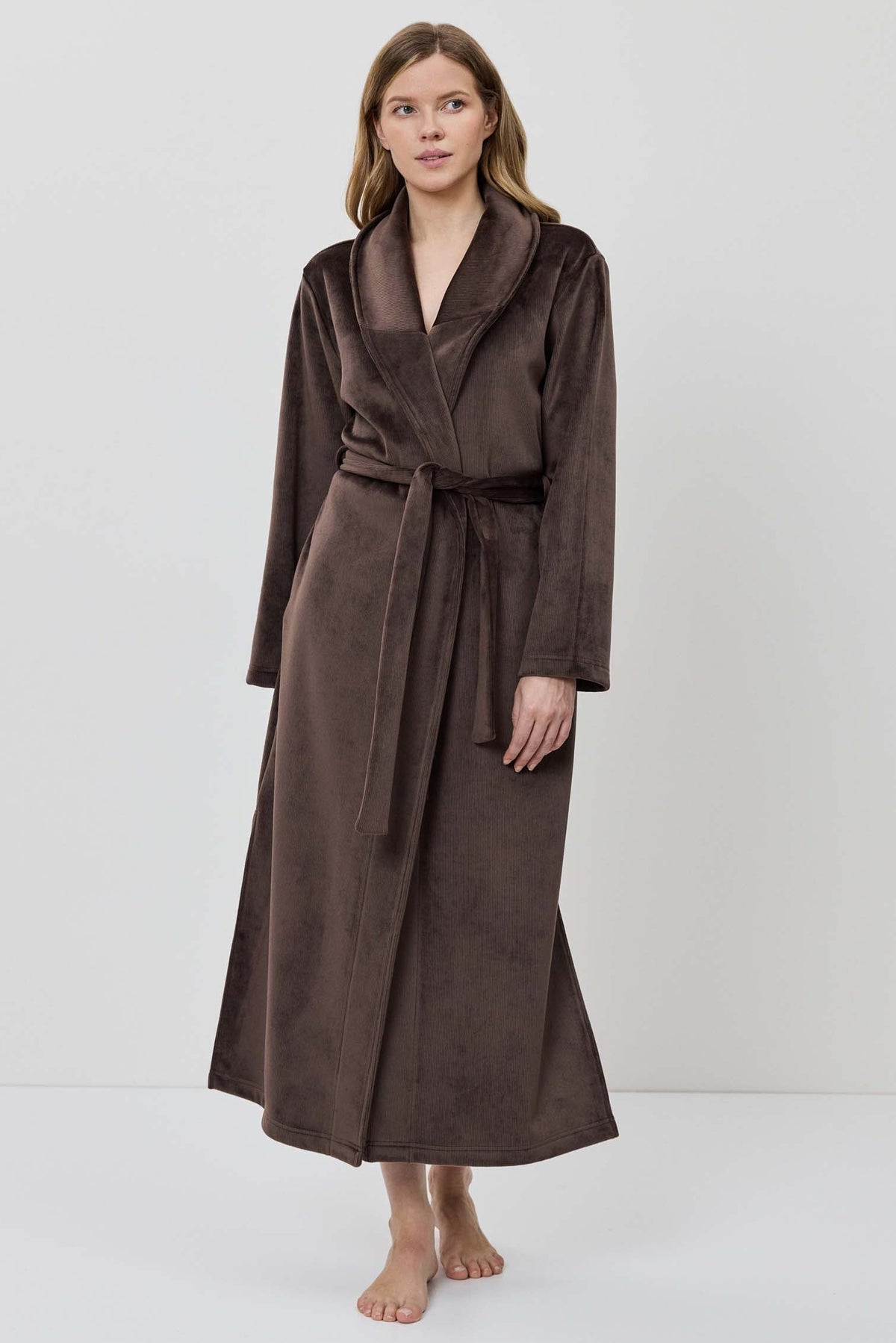 A woman wearing a long brown plush bathrobe with a tie belt.