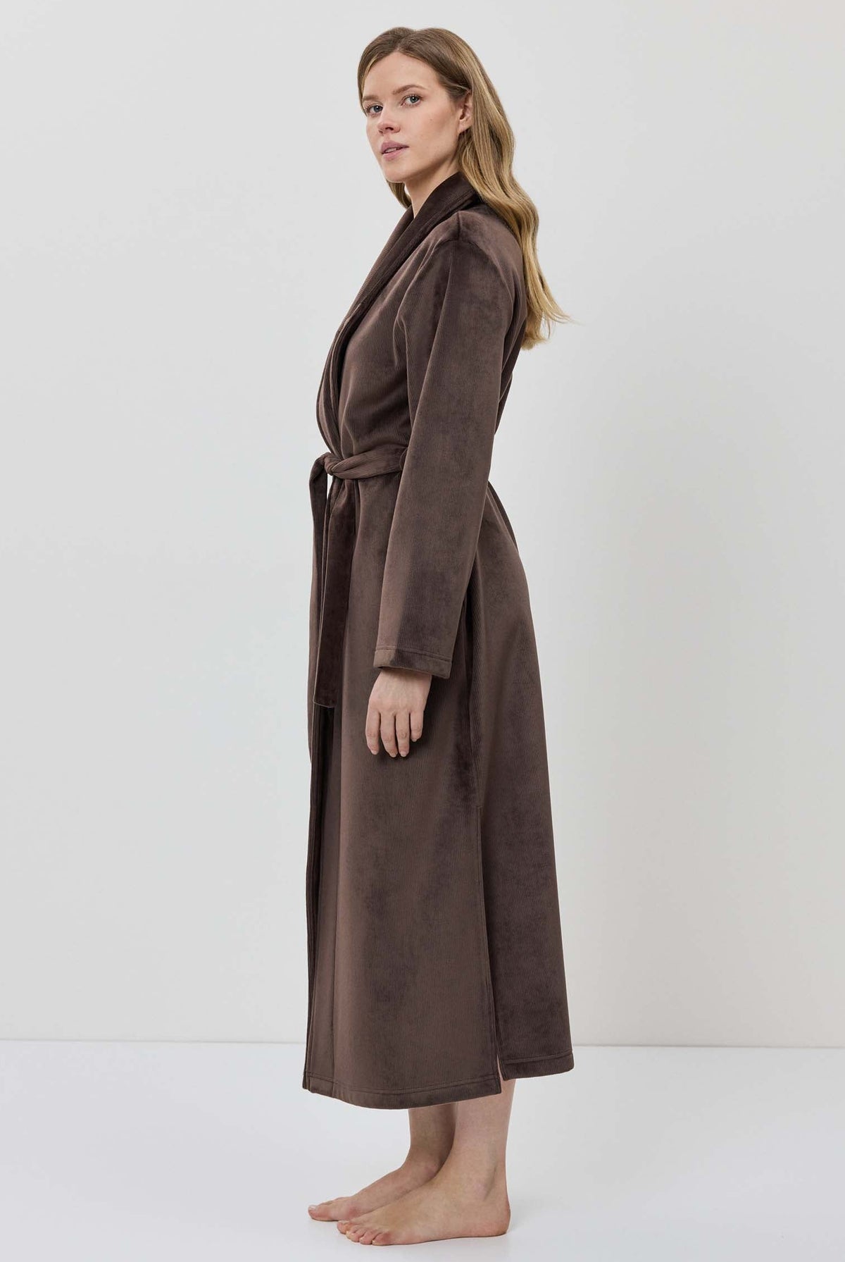 A woman wearing a long brown plush bathrobe with a tie belt.