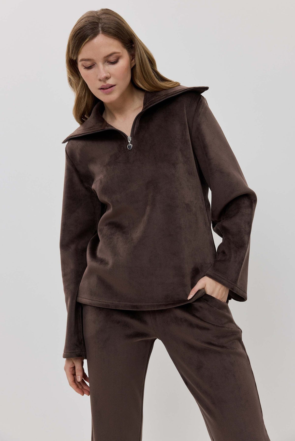 A woman modeling a matching two-piece lounge set in dark brown, featuring a long-sleeve half-zip pullover and coordinating pants.