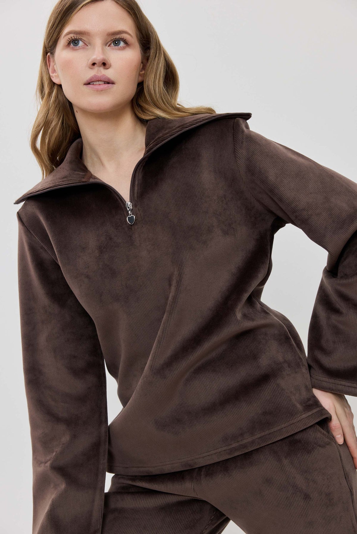A woman modeling a matching two-piece lounge set in dark brown, featuring a long-sleeve half-zip pullover and coordinating pants.