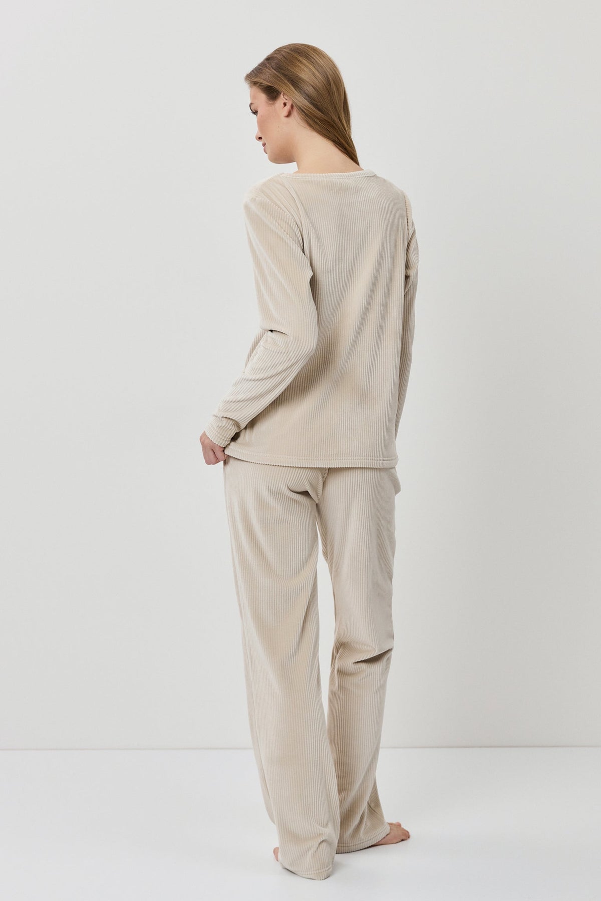 Woman wearing a beige long-sleeve top and pants on a white background