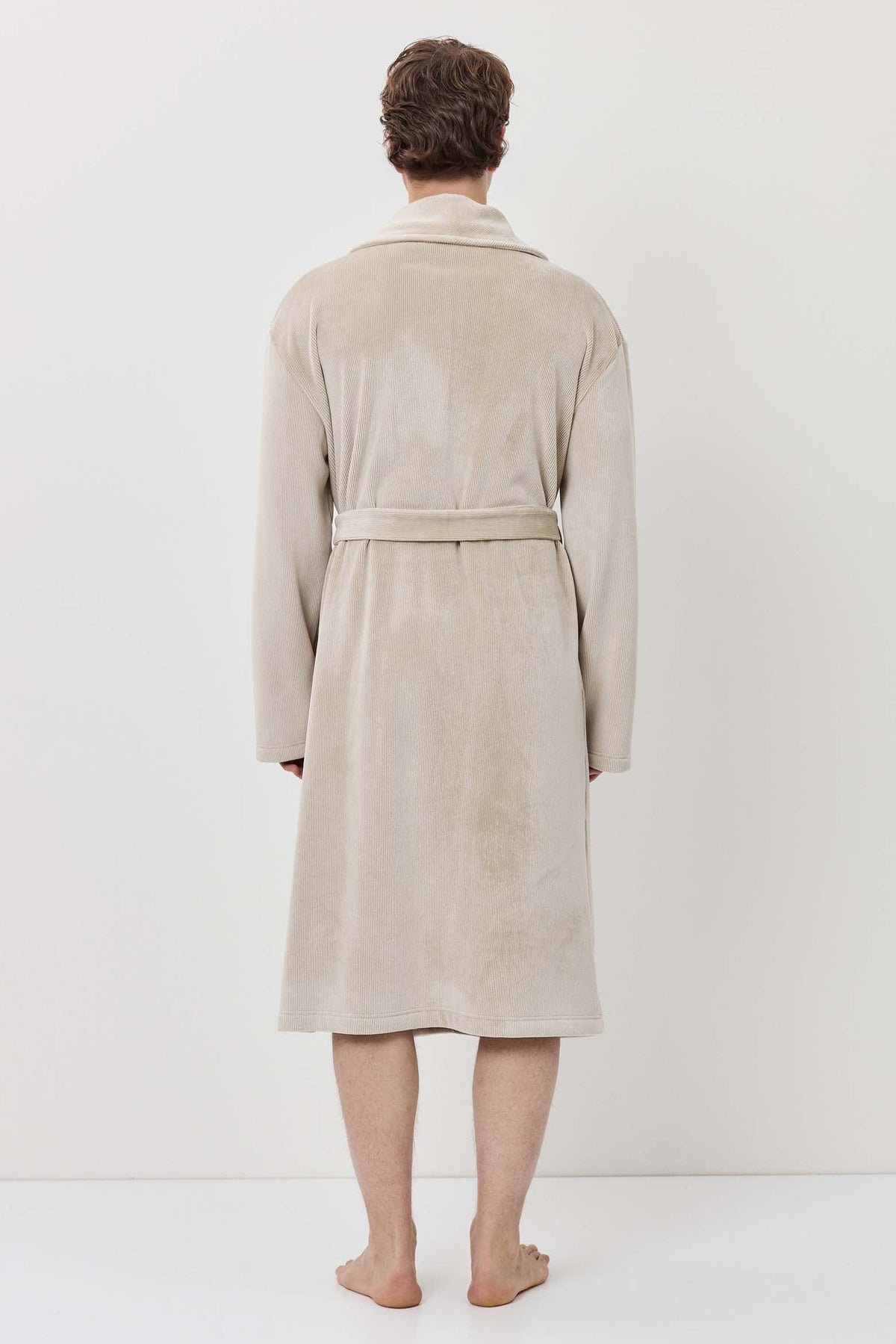 Person wearing a beige robe standing against a white background